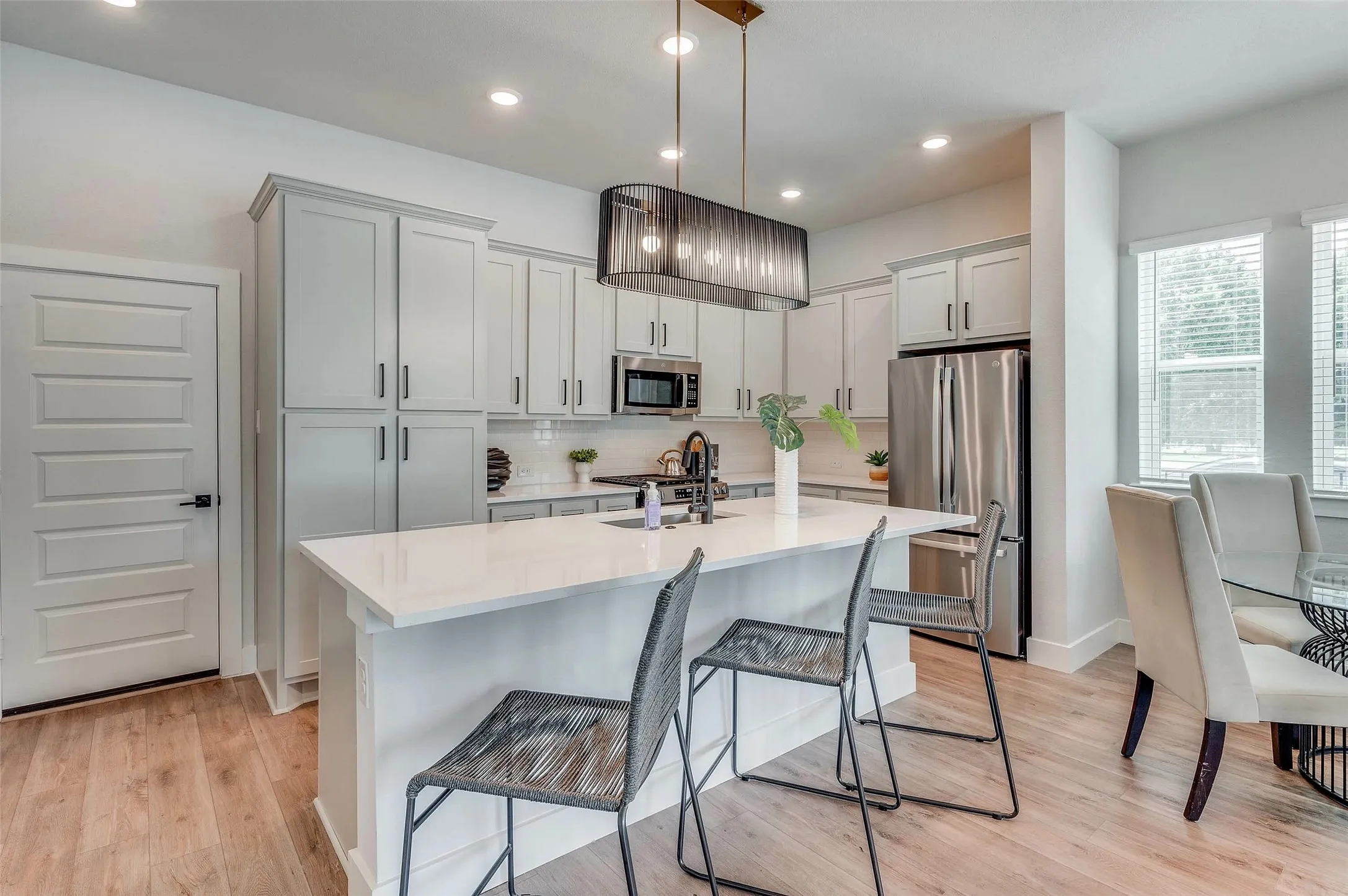 Contemporary kitchen featuring light wood-finish flooring, white cabinetry, integrated stainless steel appliances, and an island with a white countertop