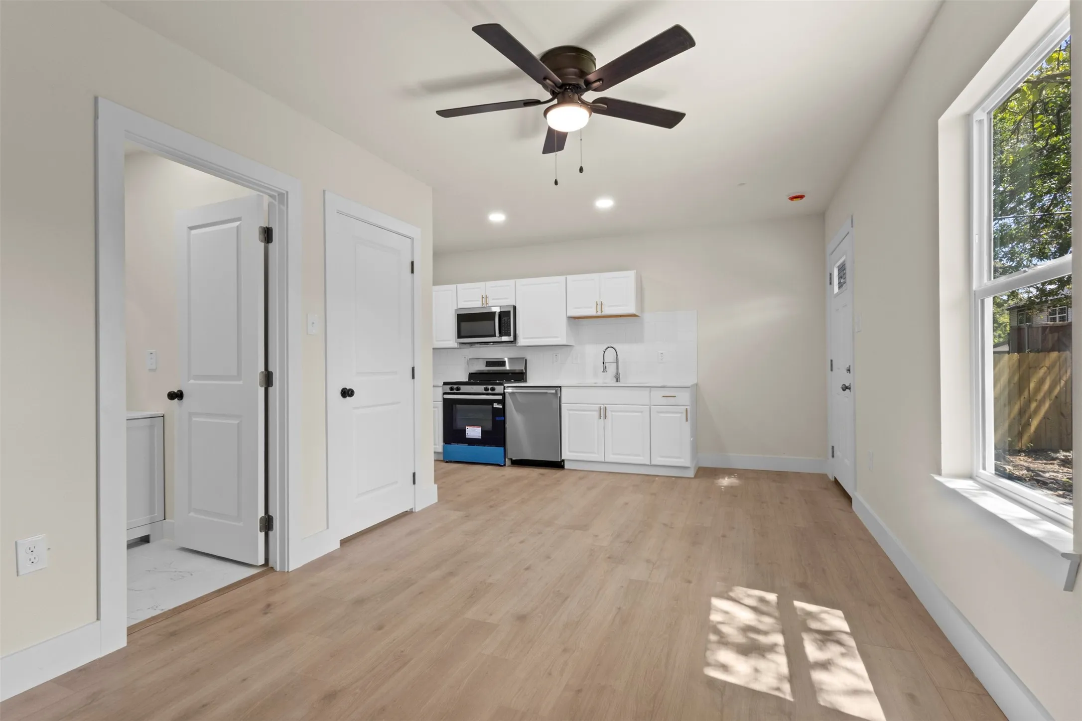 Open-concept living space with wood-finish flooring, a contemporary ceiling fan, and white kitchen cabinetry