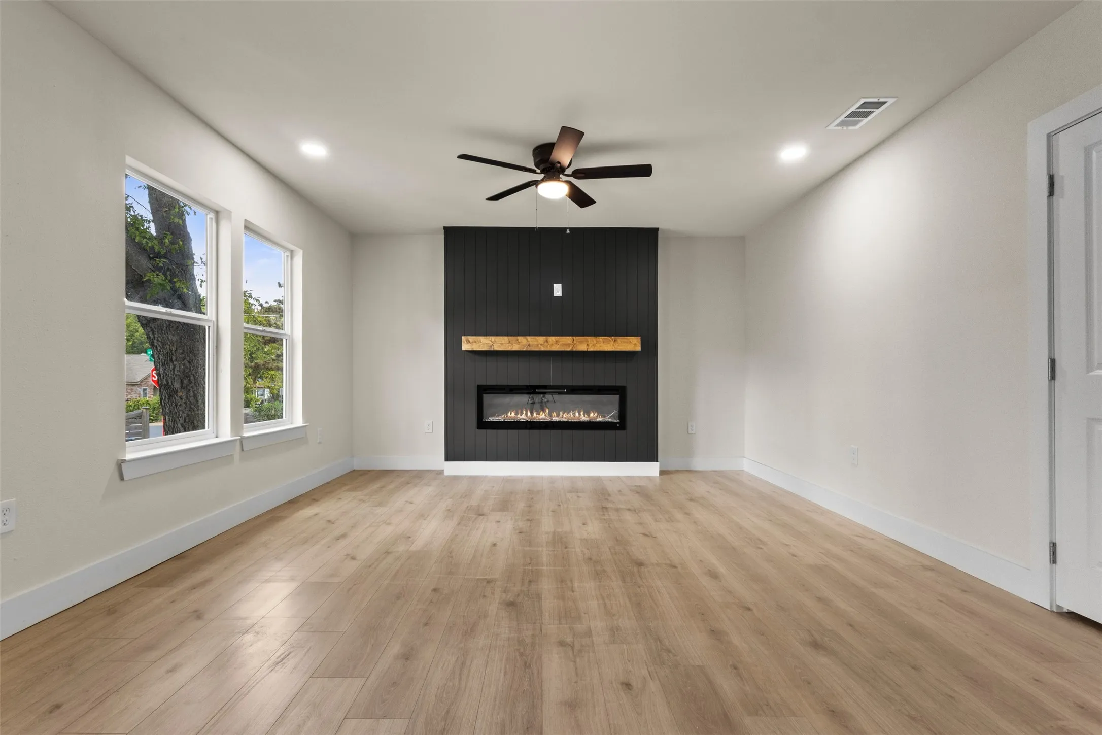 Wood-finish flooring, recessed lighting, and a dark shiplap accent wall with an electric fireplace and wood mantel