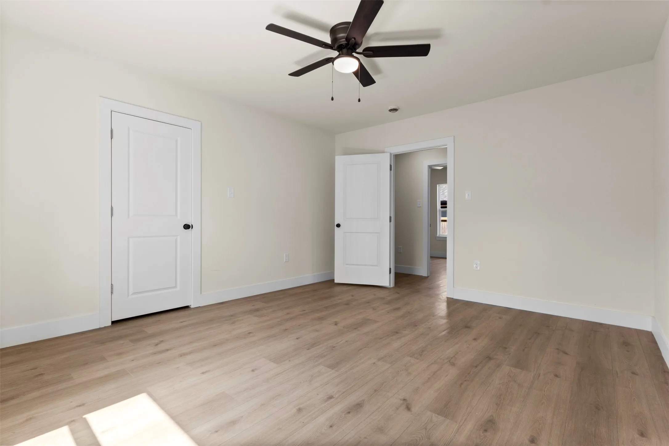 Wood-finish flooring, white trim, and a ceiling fan with light fixture