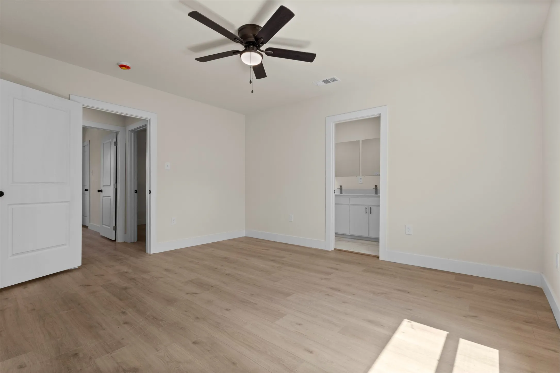 Light wood-finish flooring, white walls, dark ceiling fan with integrated lighting, and white interior doors with dark hardware