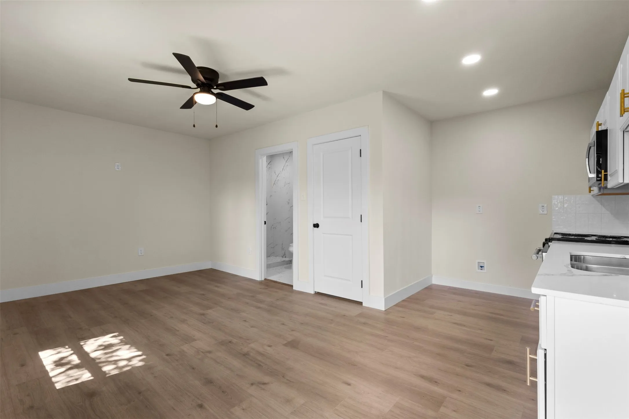 Light wood-finish flooring with a ceiling fan, recessed lighting, and a white flat-panel door