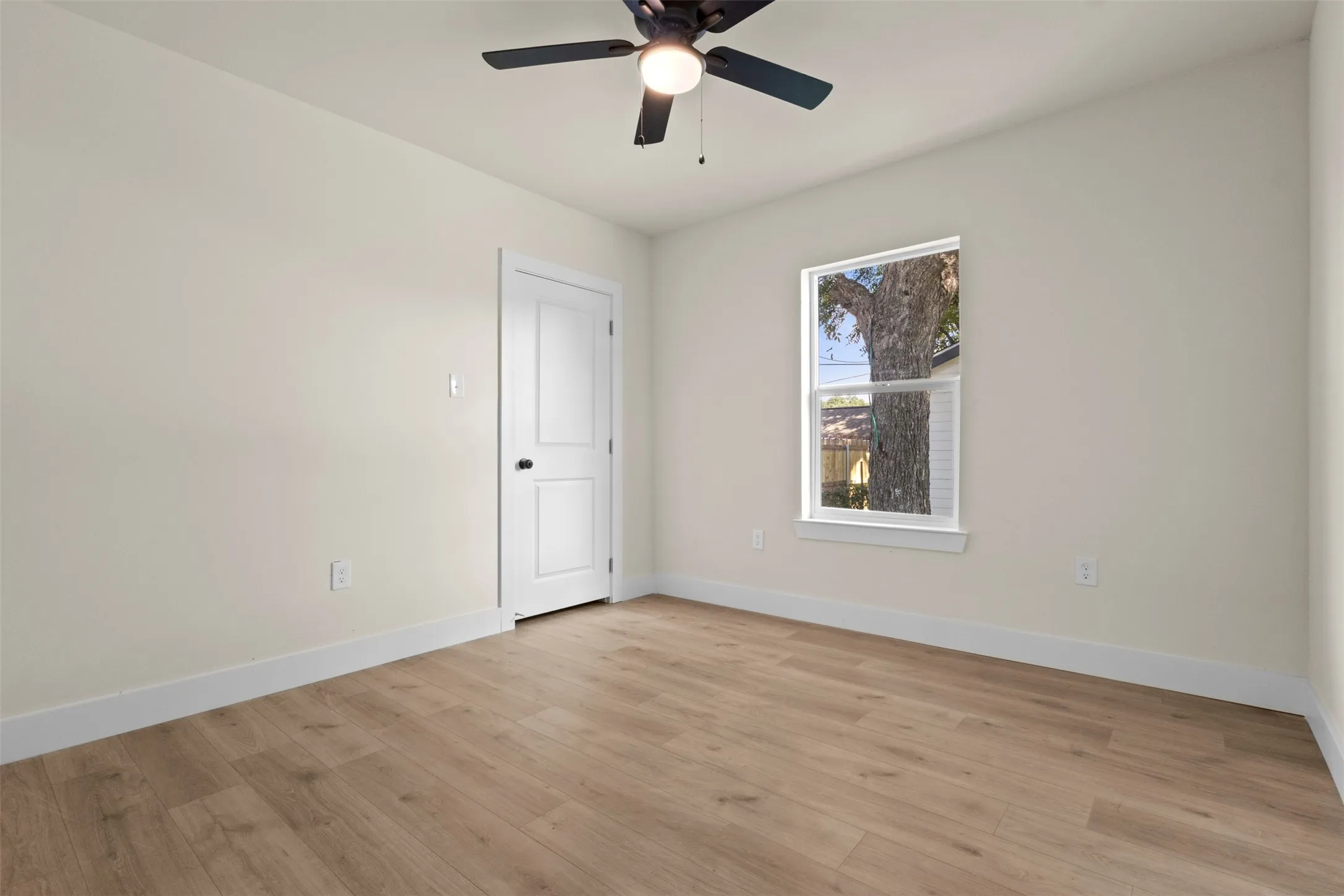 Wood-finish flooring, neutral wall tones, ceiling fan with light, white trim, and a paneled door