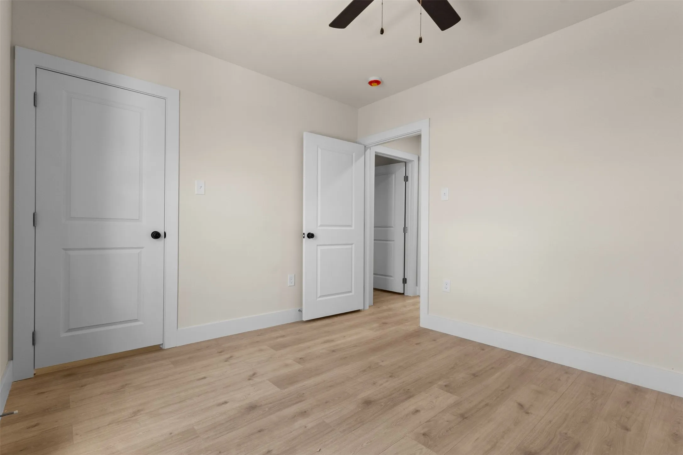 Light wood-finish flooring, neutral wall paint, white trim, and a ceiling fan