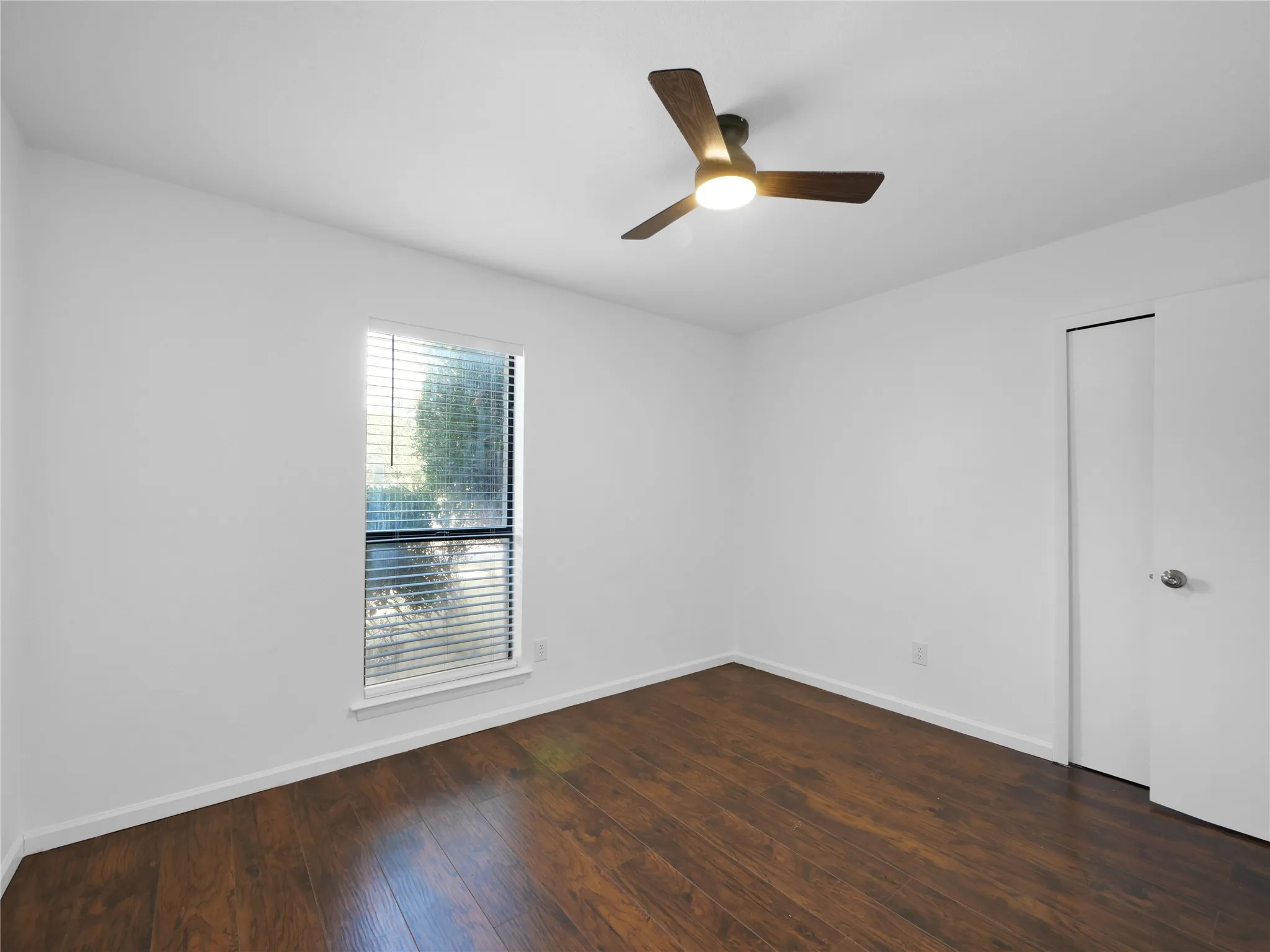 Wood-finish flooring, white walls, and a window with blinds