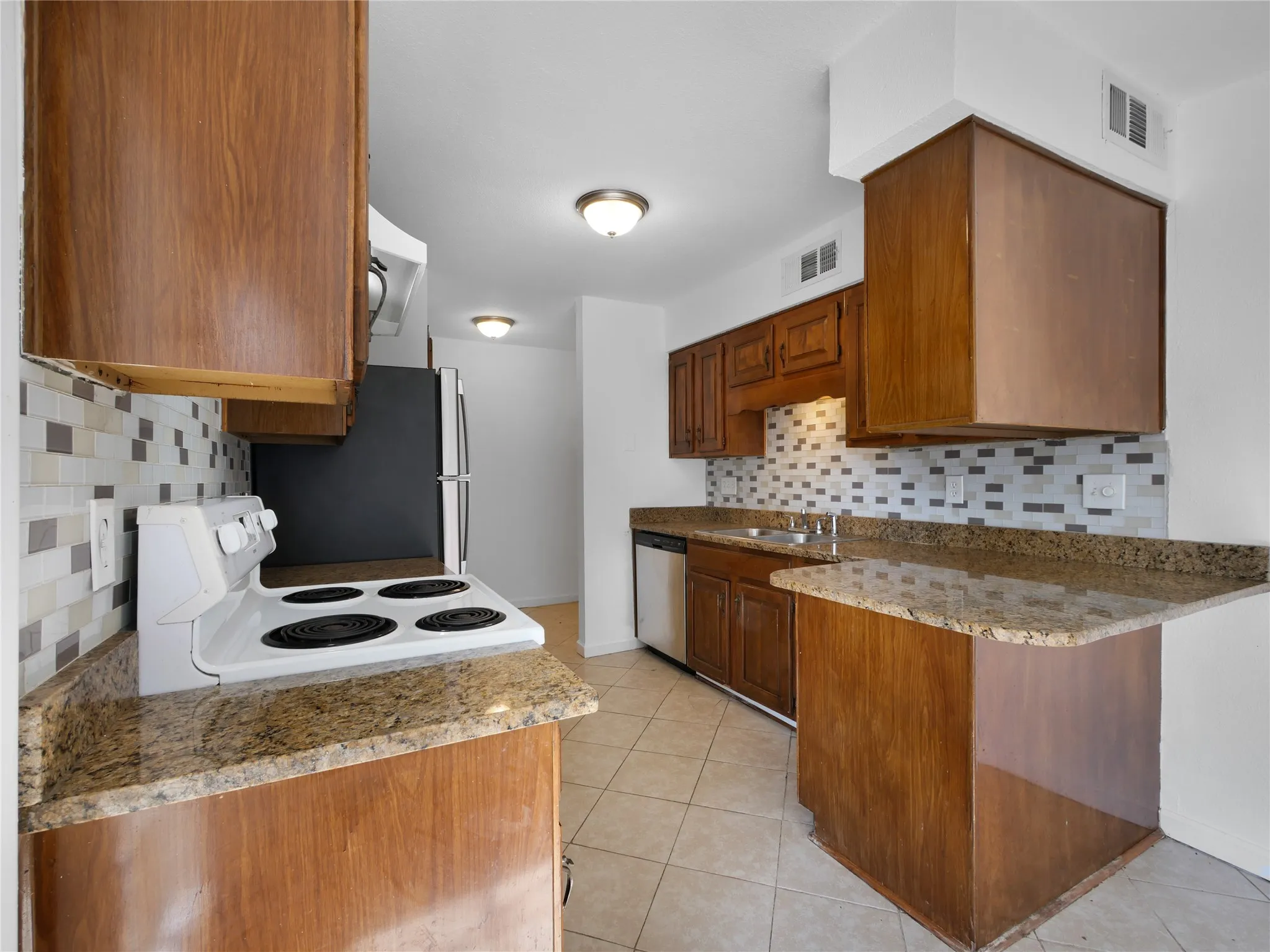Kitchen featuring wood-finish cabinetry, patterned tile backsplash, granite-style countertops, and tile flooring