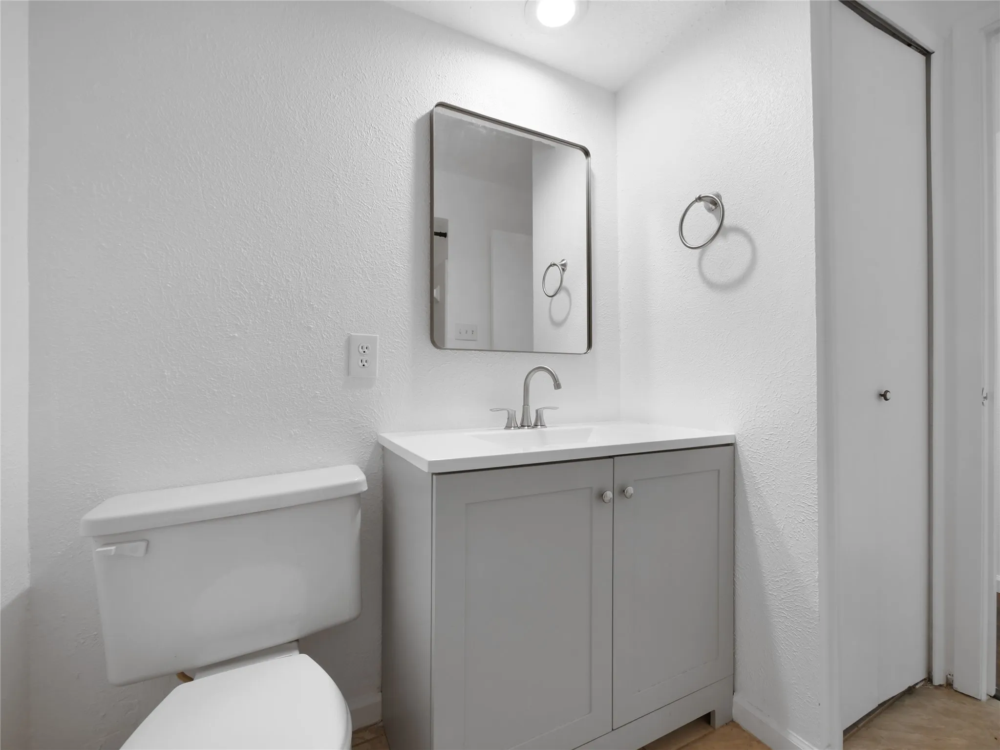 Bathroom featuring a white toilet, gray vanity with white countertop, rectangular mirror, and recessed lighting