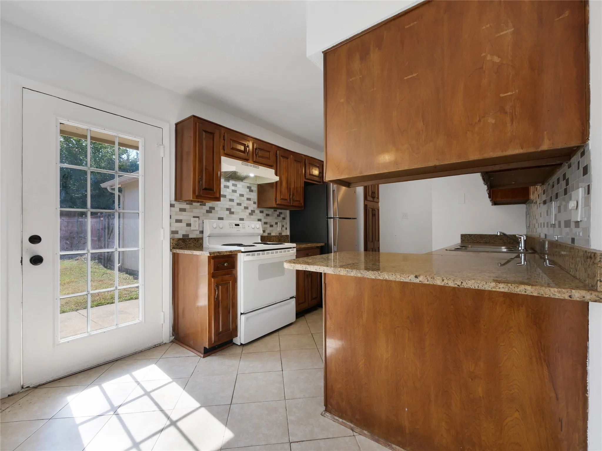 Kitchen featuring wood cabinetry, a tiled backsplash, and light-toned tile flooring