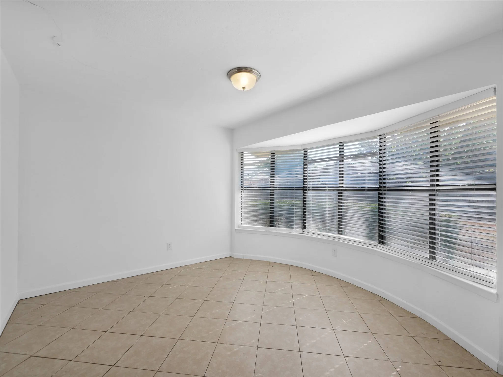 Curved bay window with horizontal blinds, tiled flooring, and a flush-mount ceiling light fixture