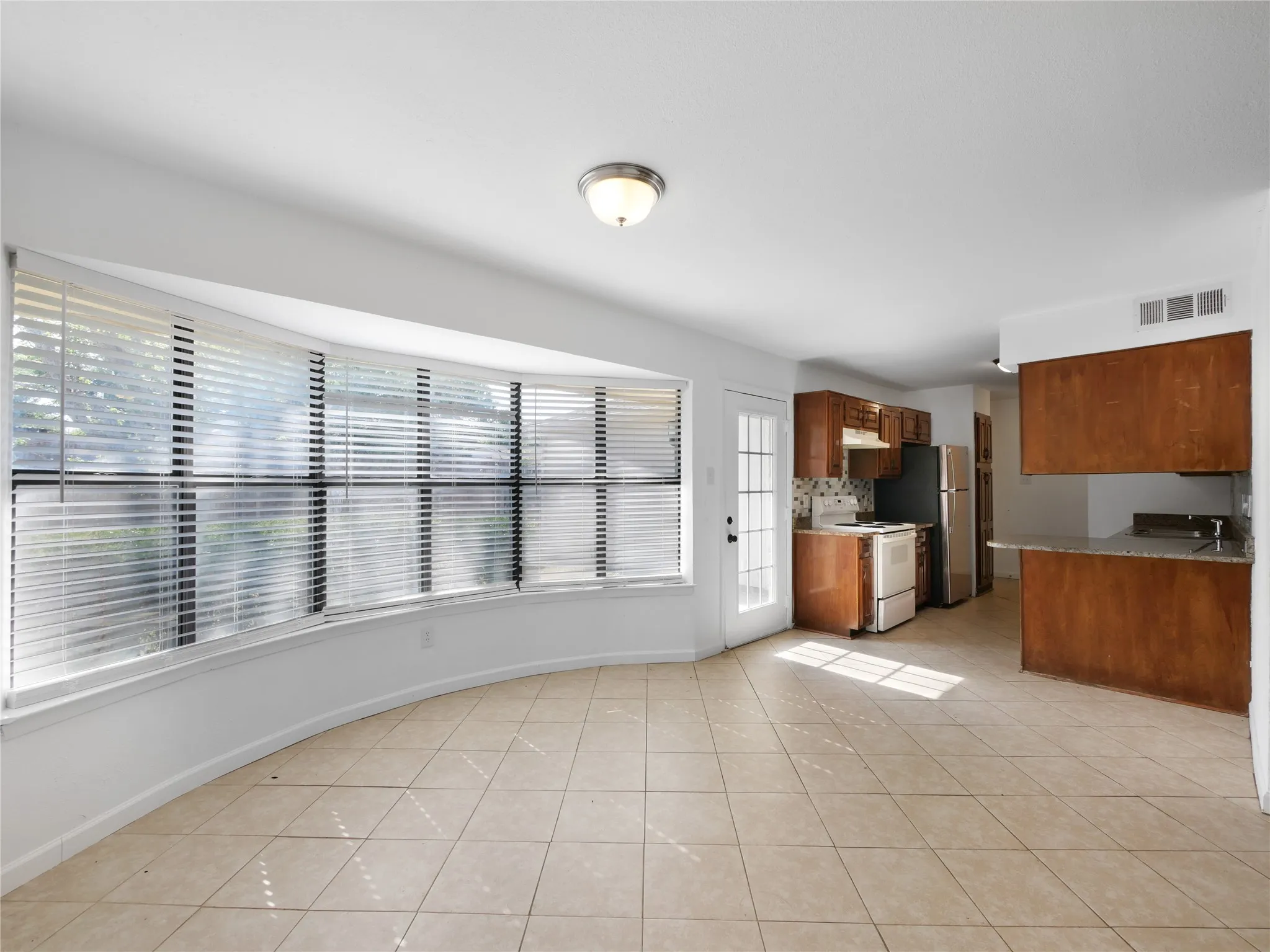 Open-concept living space featuring a curved bay window, ceramic tile flooring, and an attached kitchen with wood-finish cabinetry