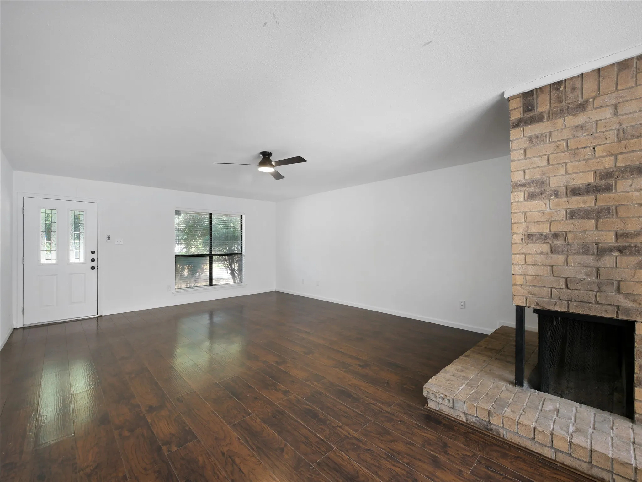 Wood-finish flooring throughout, with a brick-surround fireplace, and a ceiling fan
