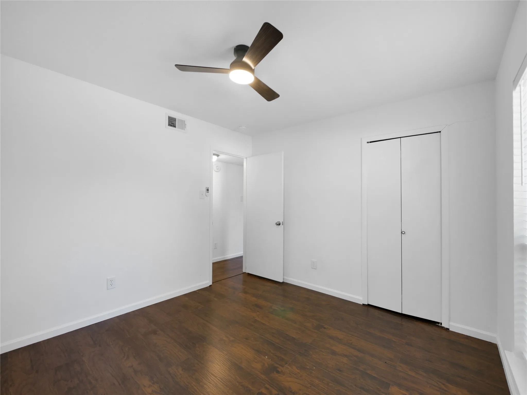 Dark wood-finish flooring, white walls, ceiling-mounted light fixture with fan, bi-fold closet doors, and recessed window