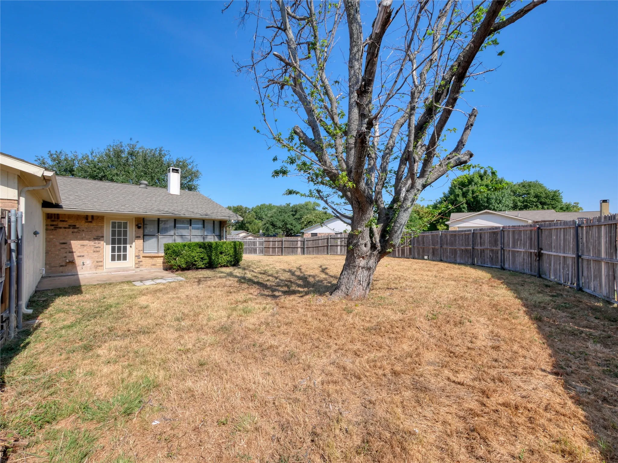 Expansive backyard featuring a mature tree, privacy fencing, and a brick-faced exterior with a patio