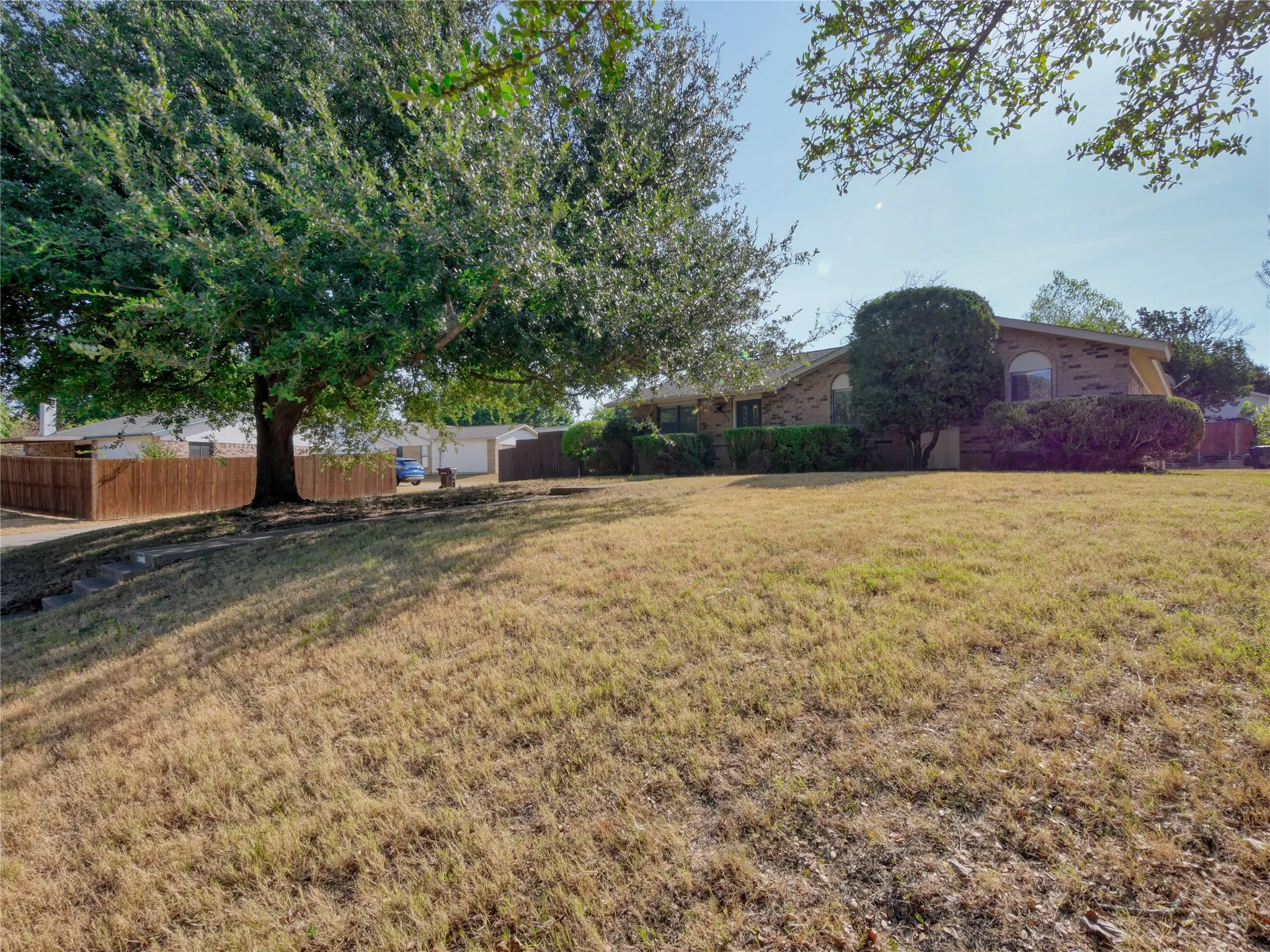 Brick exterior home with arched windows, mature landscaping, and an expansive front yard