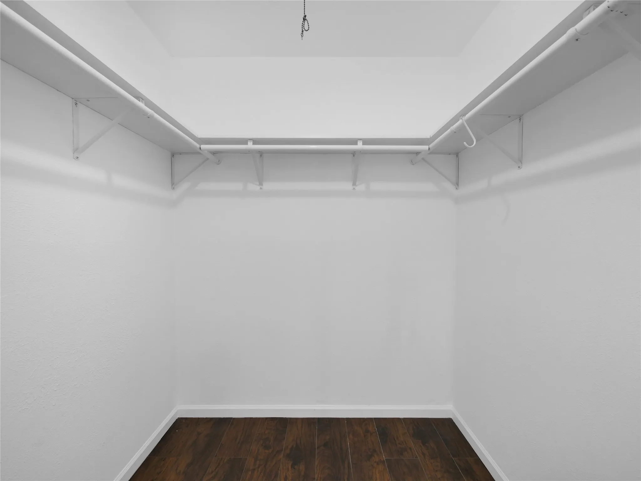 Walk-in closet featuring built-in shelving, hanging rods, and dark wood-finish flooring