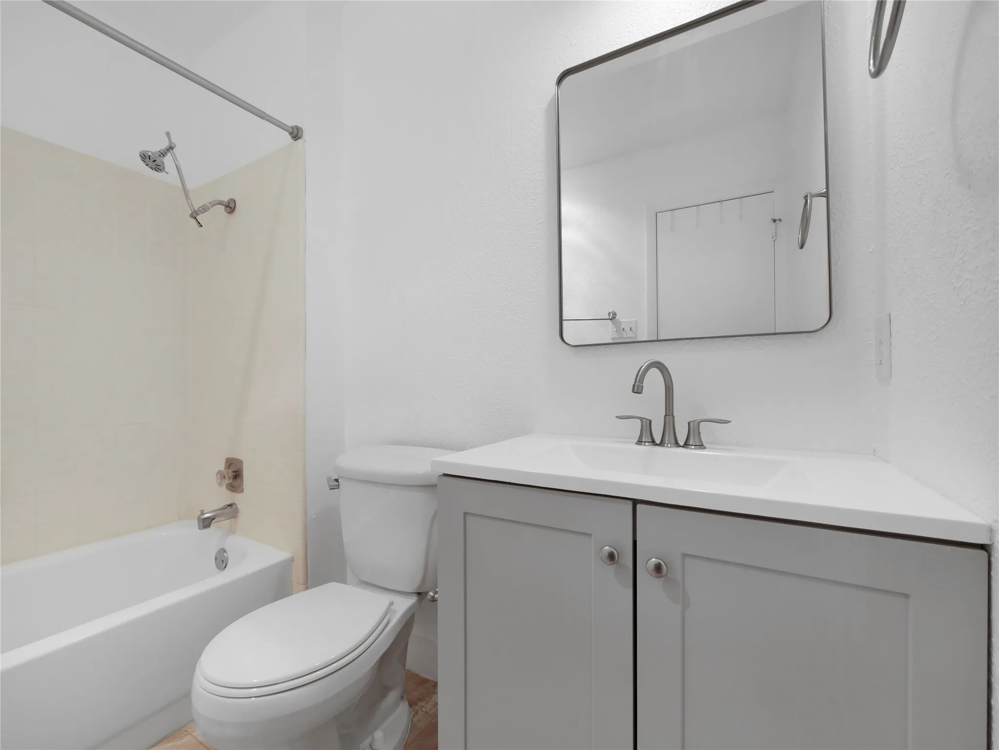White tub and shower combination with chrome fixtures, light gray vanity with white countertop, integrated sink, and an arched rectangular mirror