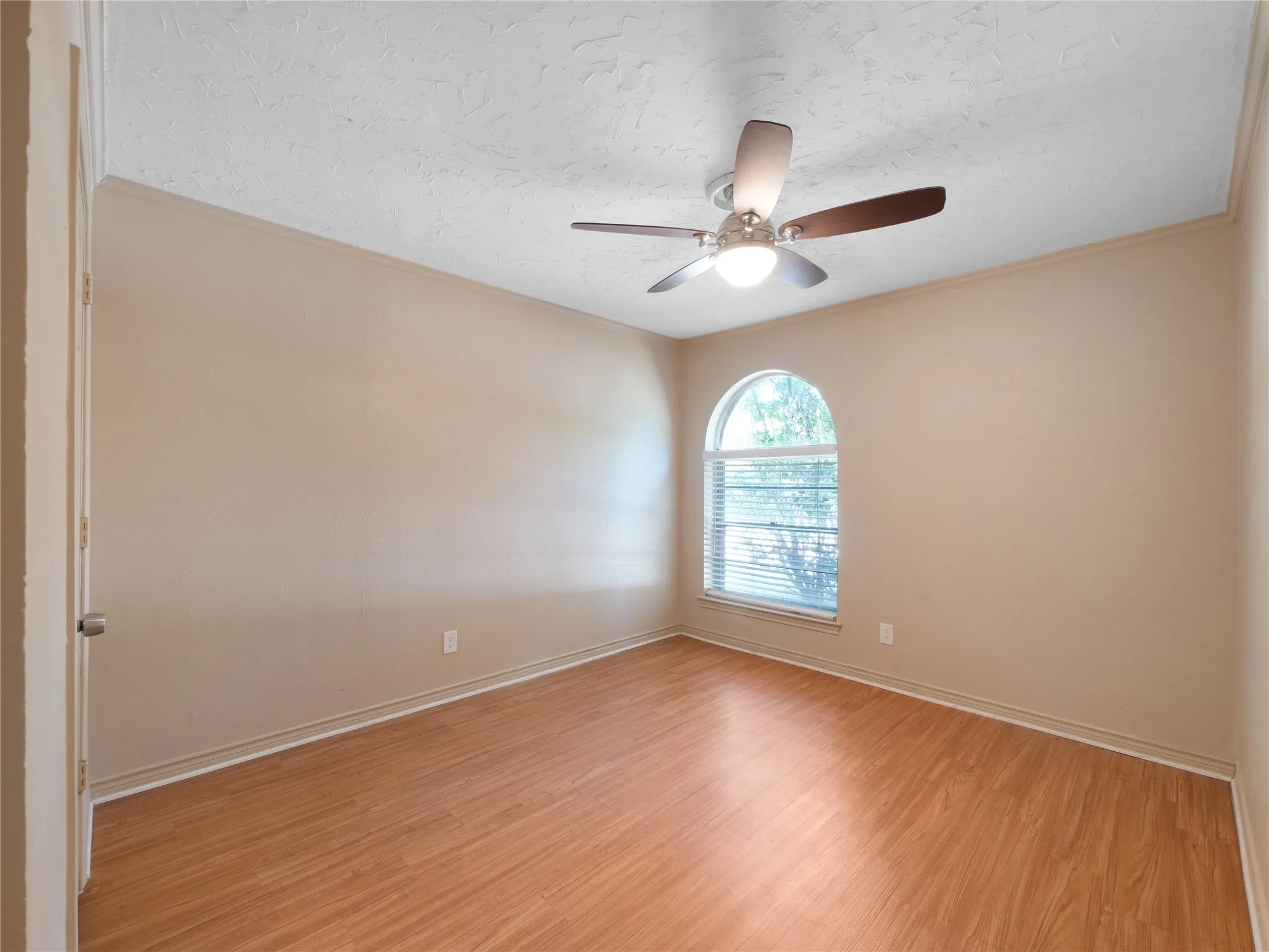 Wood-finish flooring, arched window with blinds, ceiling fan with integrated lighting, and crown molding