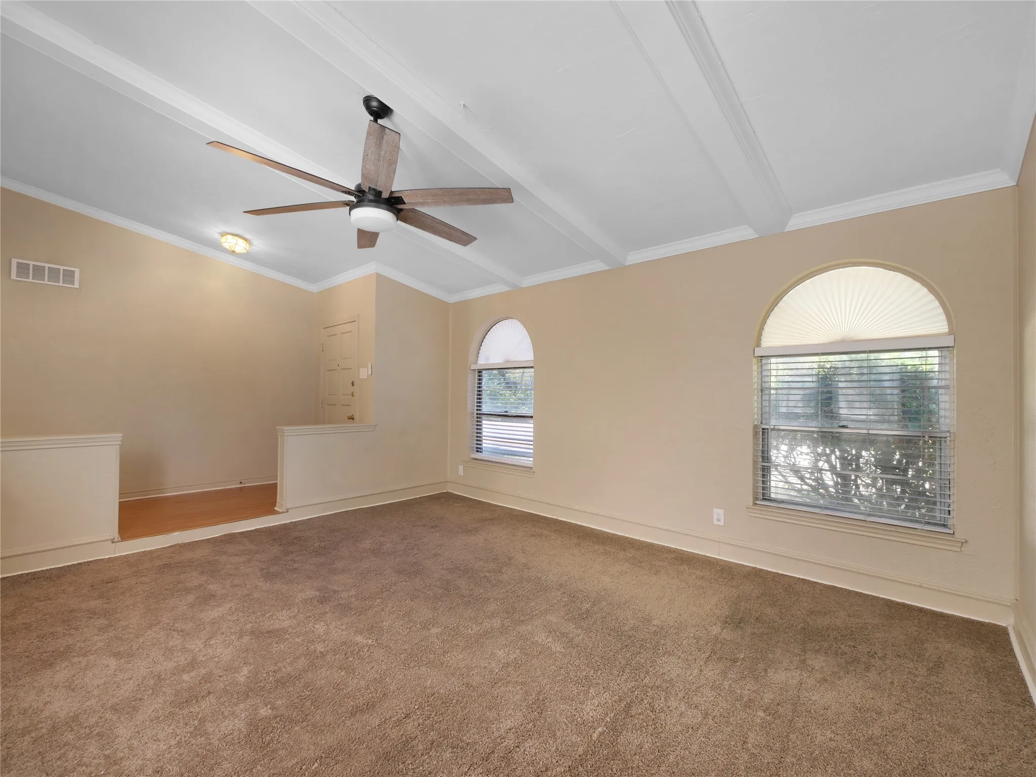 Vaulted ceiling with exposed beams, wood-finish ceiling fan, and arched windows