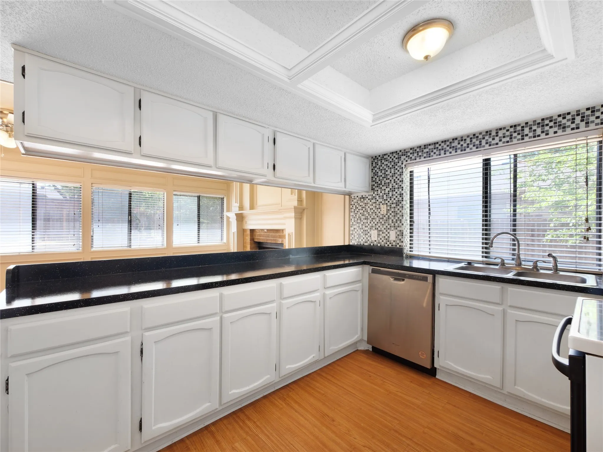 White cabinetry with black countertops, mosaic tile backsplash, and wood-finish flooring