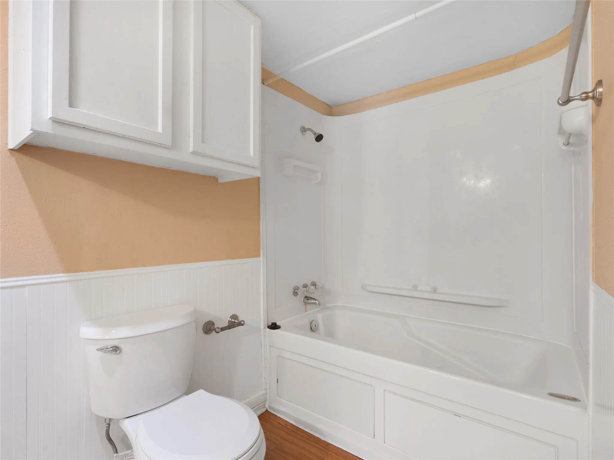 White paneled wainscoting, white wall-mounted cabinetry, white toilet, and a white bathtub with shower
