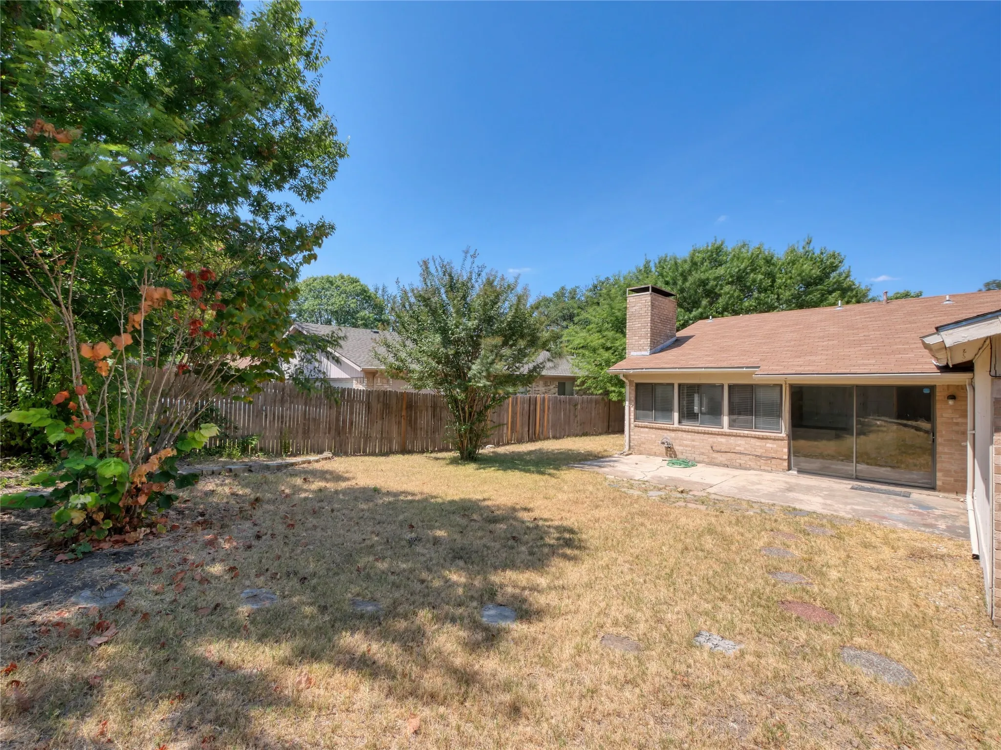 Expansive backyard with a wood privacy fence, mature trees, a screened-in porch, and a stone patio