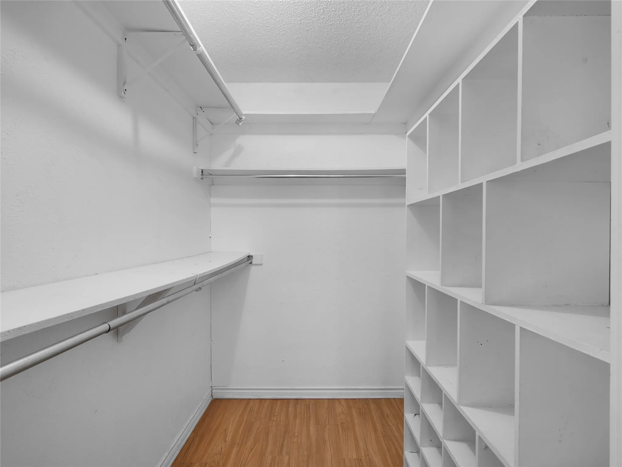 Walk-in closet with multiple hanging rods, built-in shelving, and wood-finish flooring