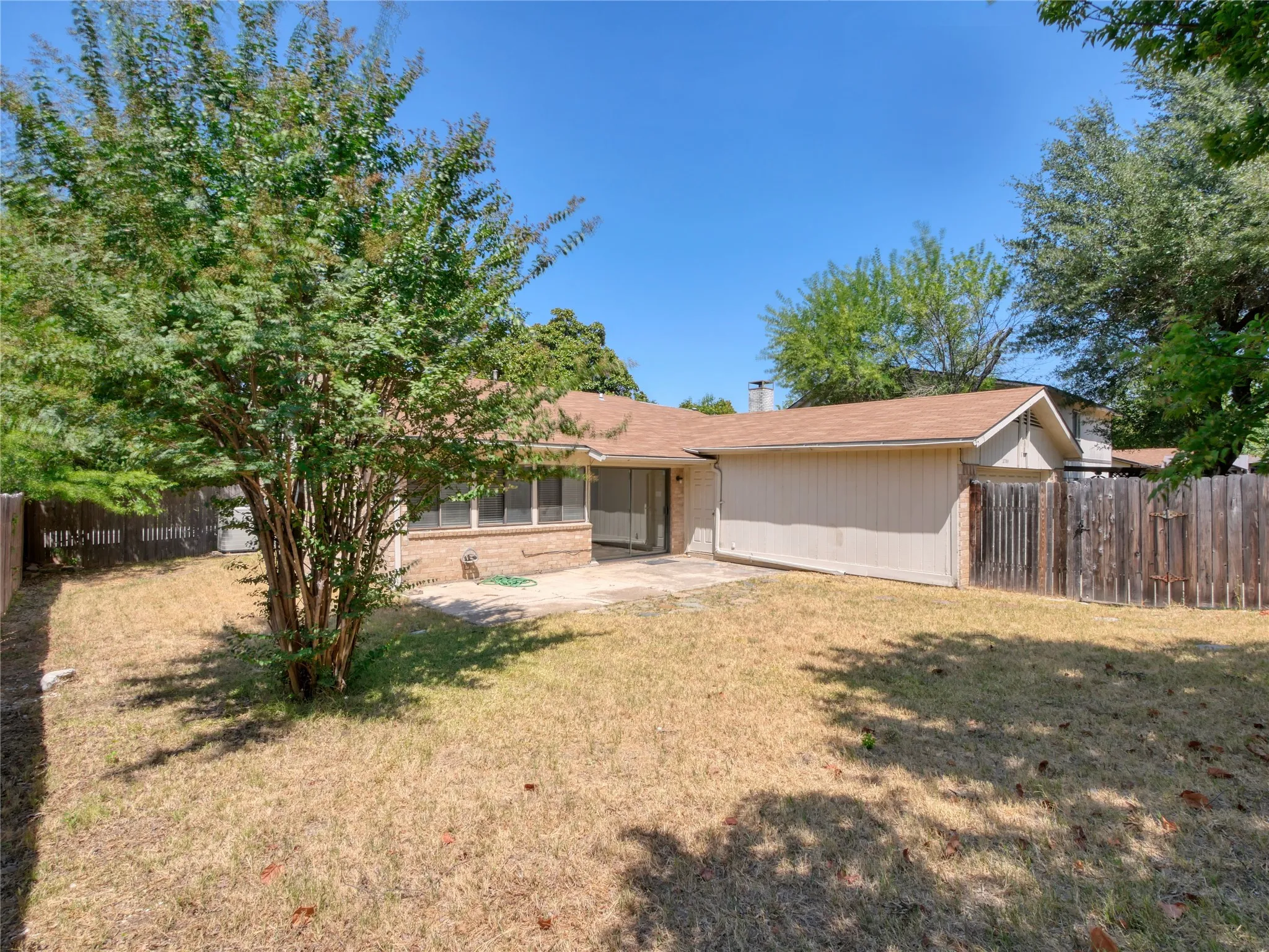 Expansive backyard featuring a mature tree, a paved patio area, brick exterior siding, and a wood privacy fence
