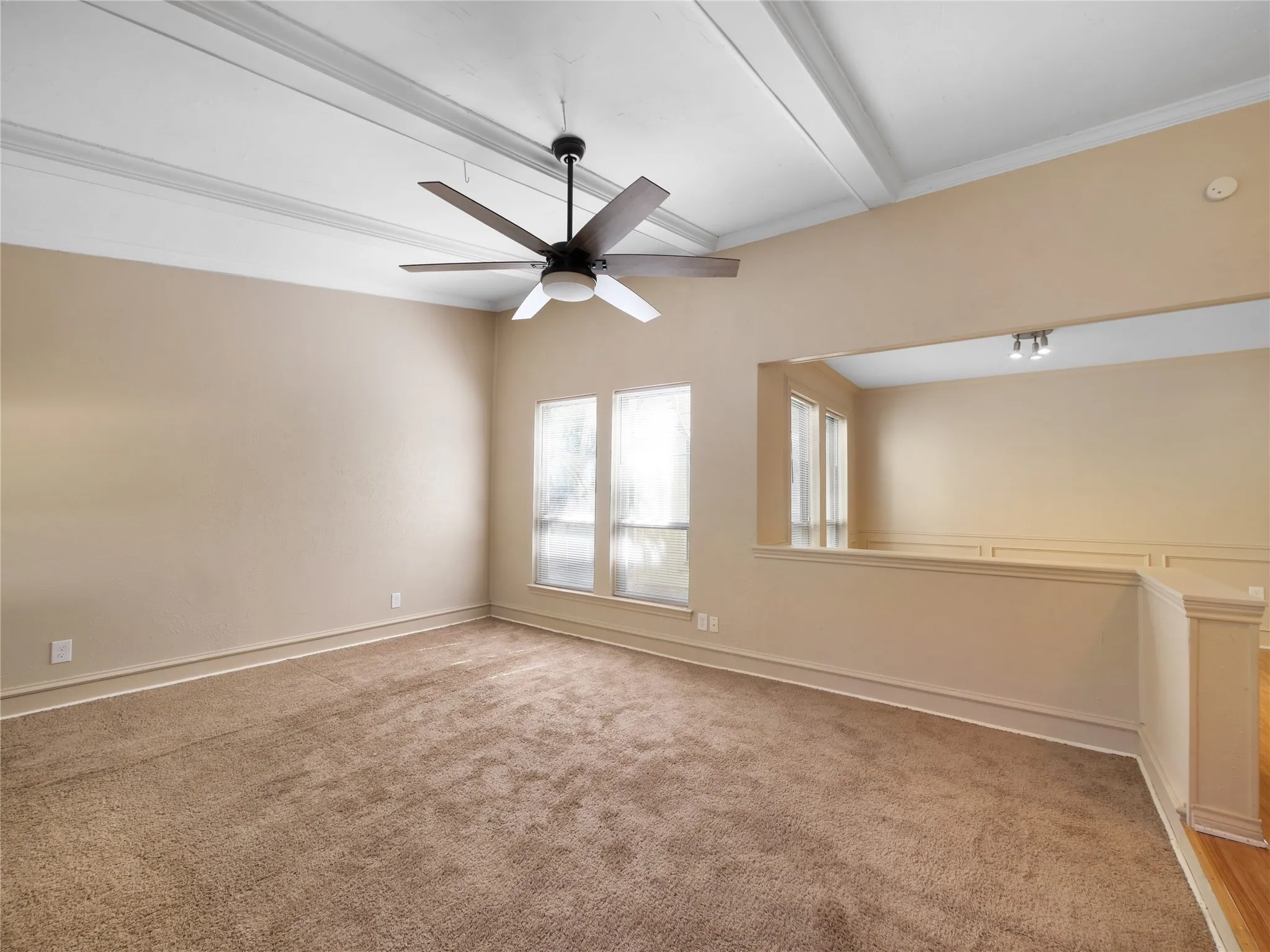 Vaulted ceiling with decorative beams, large windows, ceiling fan with integrated lighting, wainscoting, and wood-finish flooring
