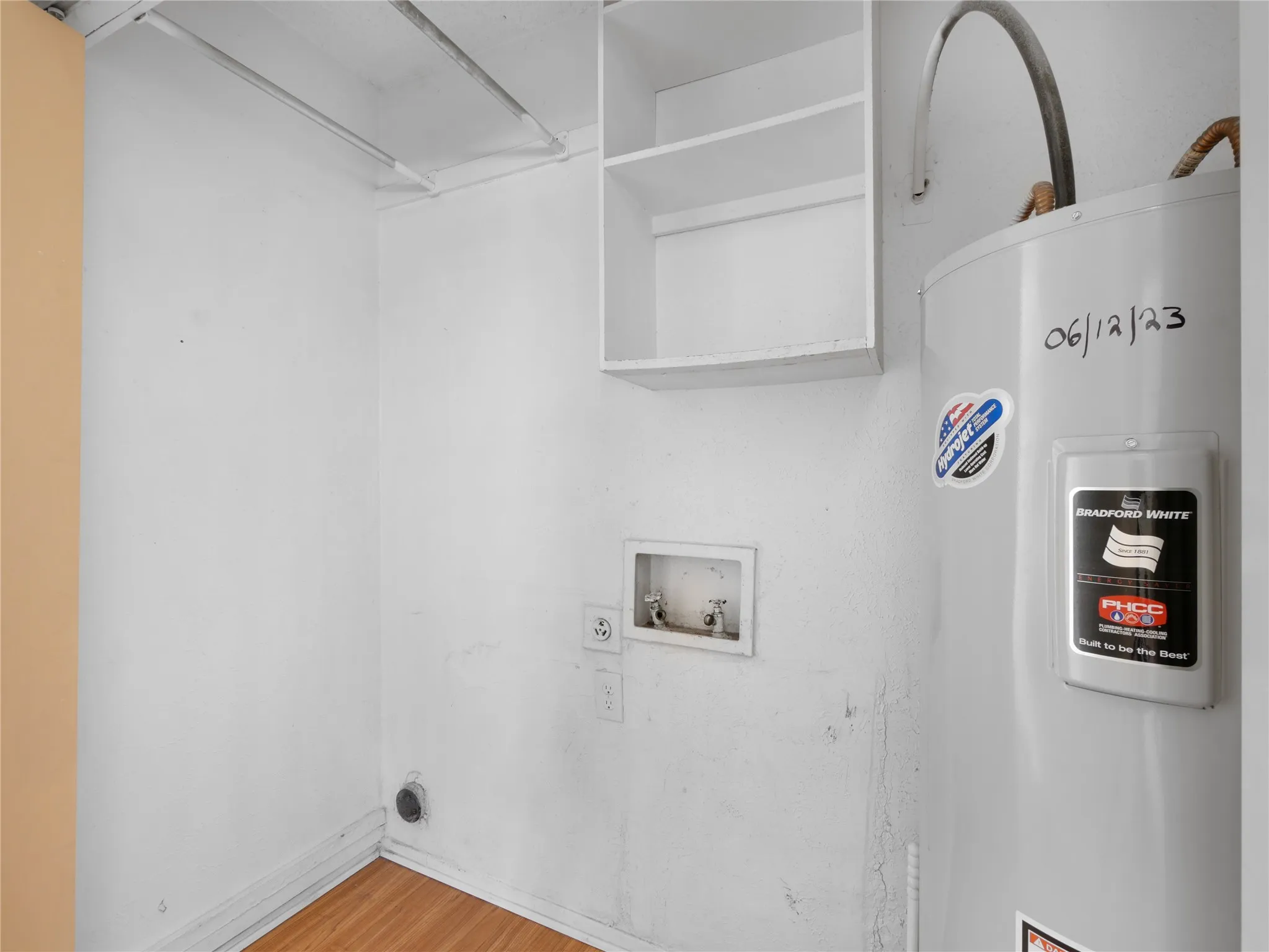 Utility area featuring built-in shelving, water heater, wood-finish flooring, and laundry hookups