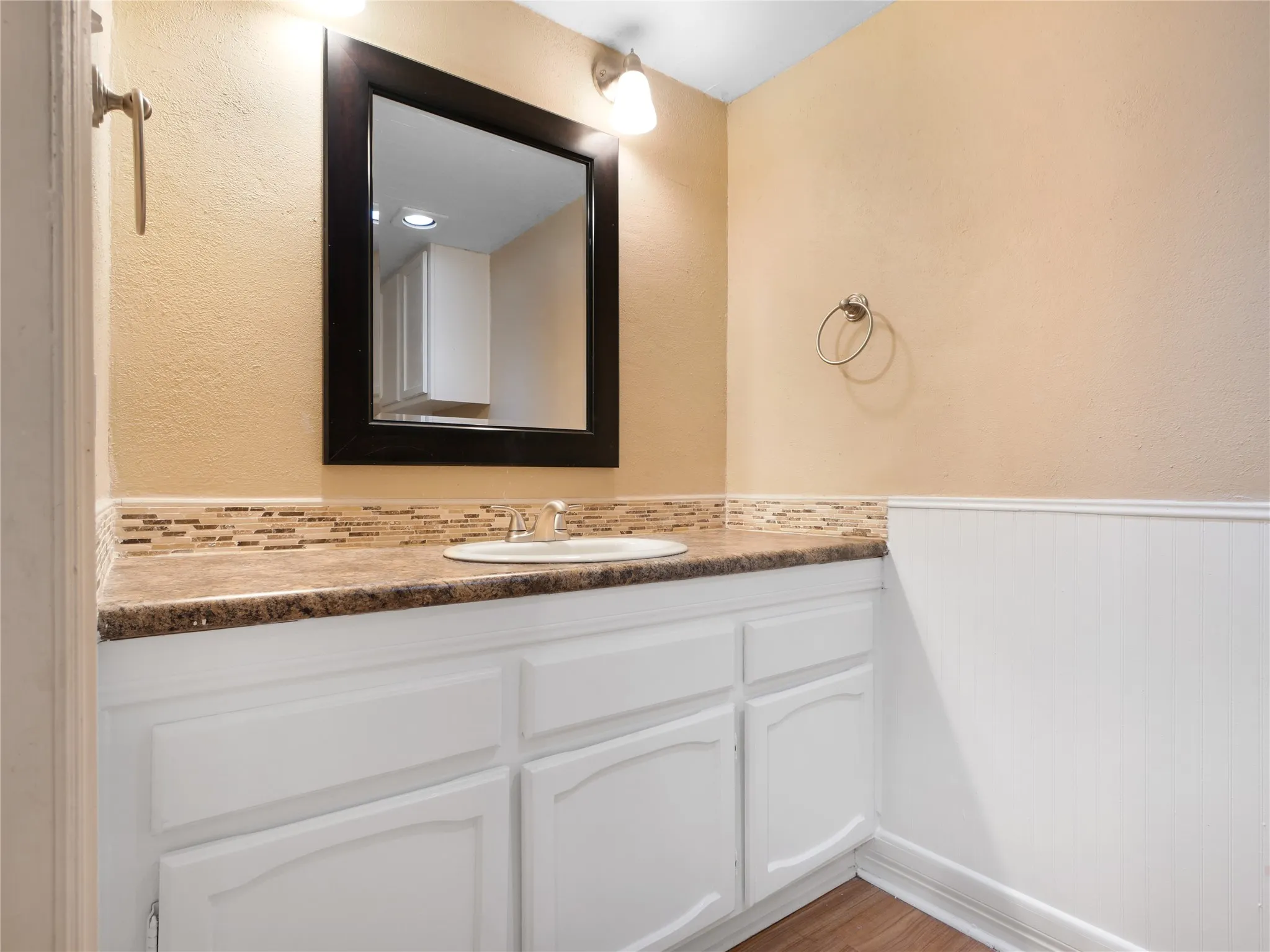 White vanity with recessed panel doors, drop-in sink, and a dark-framed mirror