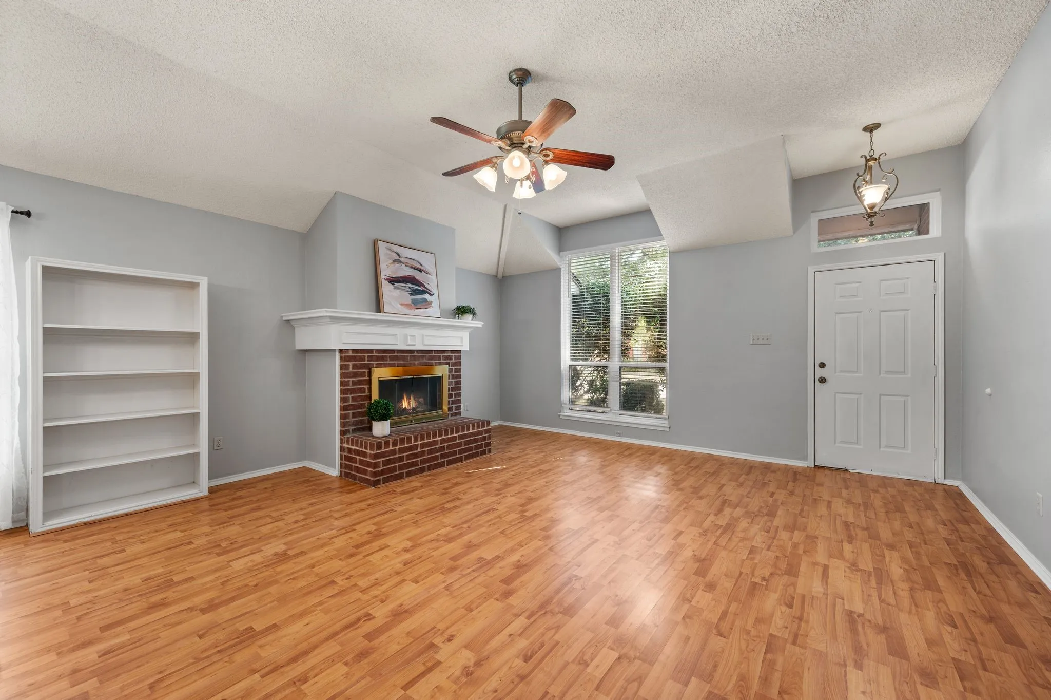 Light-filled living room features warm wood-look flooring, a vaulted ceiling, built-ins & a brick fireplace.