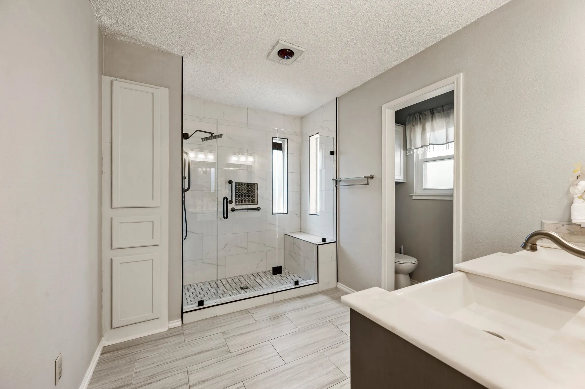 Updated primary bath features an oversized frameless shower, modern tilework, a built-in bench & rainfall showerhead.