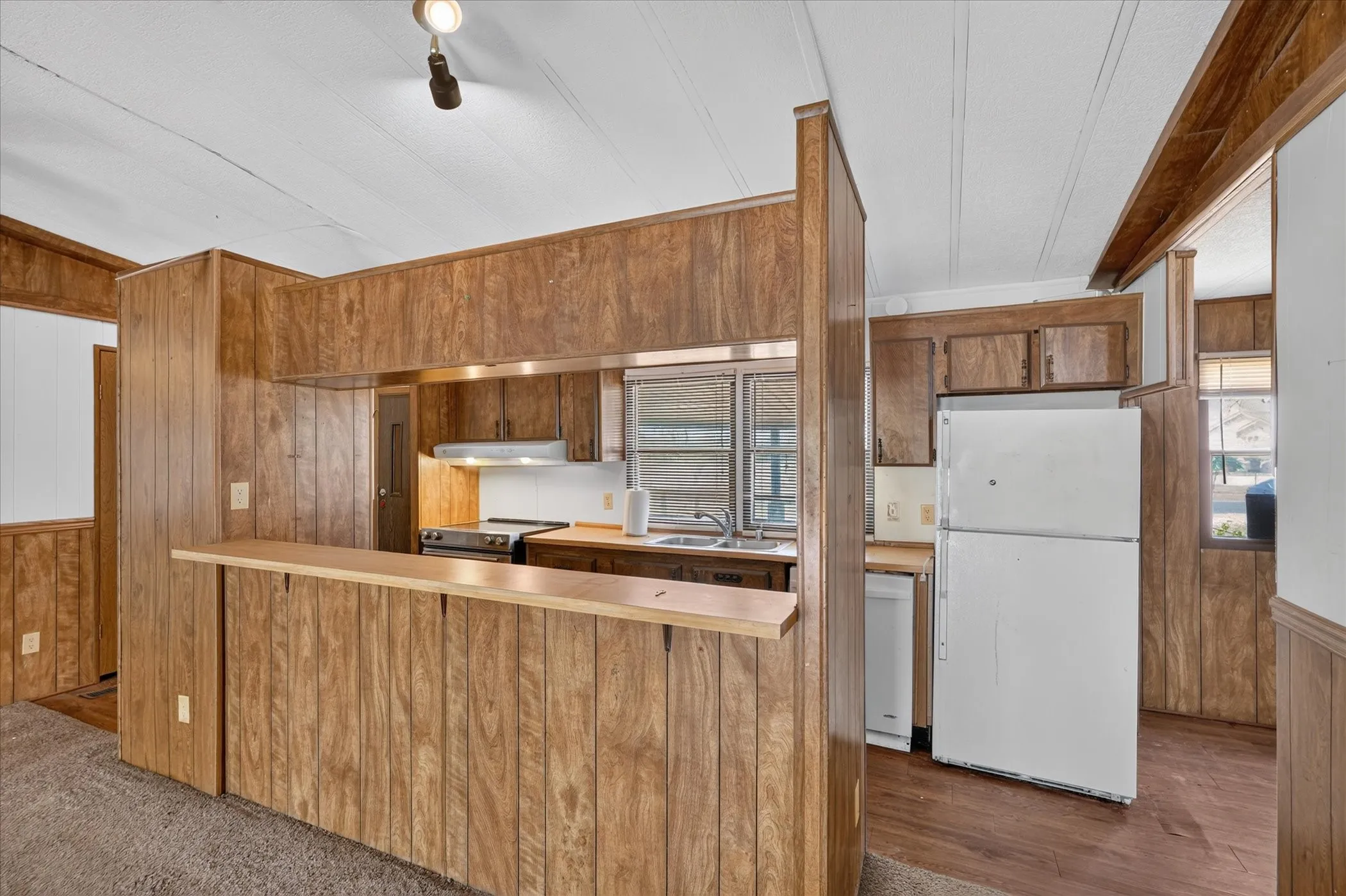 Kitchen featuring wood-panel walls, wood-finish flooring, wood cabinetry, built-in stainless steel oven, and a double-basin stainless steel sink