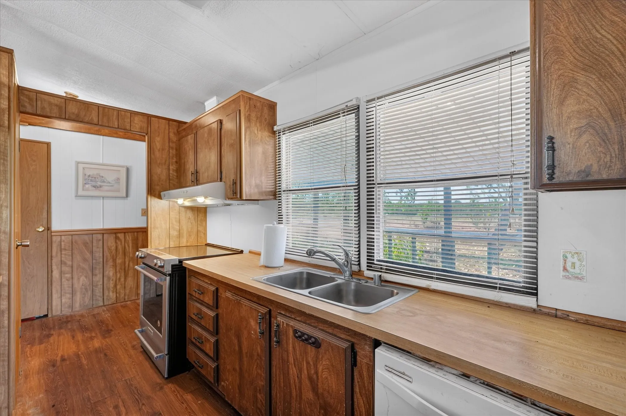 Wood-finish flooring, wood paneling, stainless steel range, dual basin sink, and ample cabinet storage