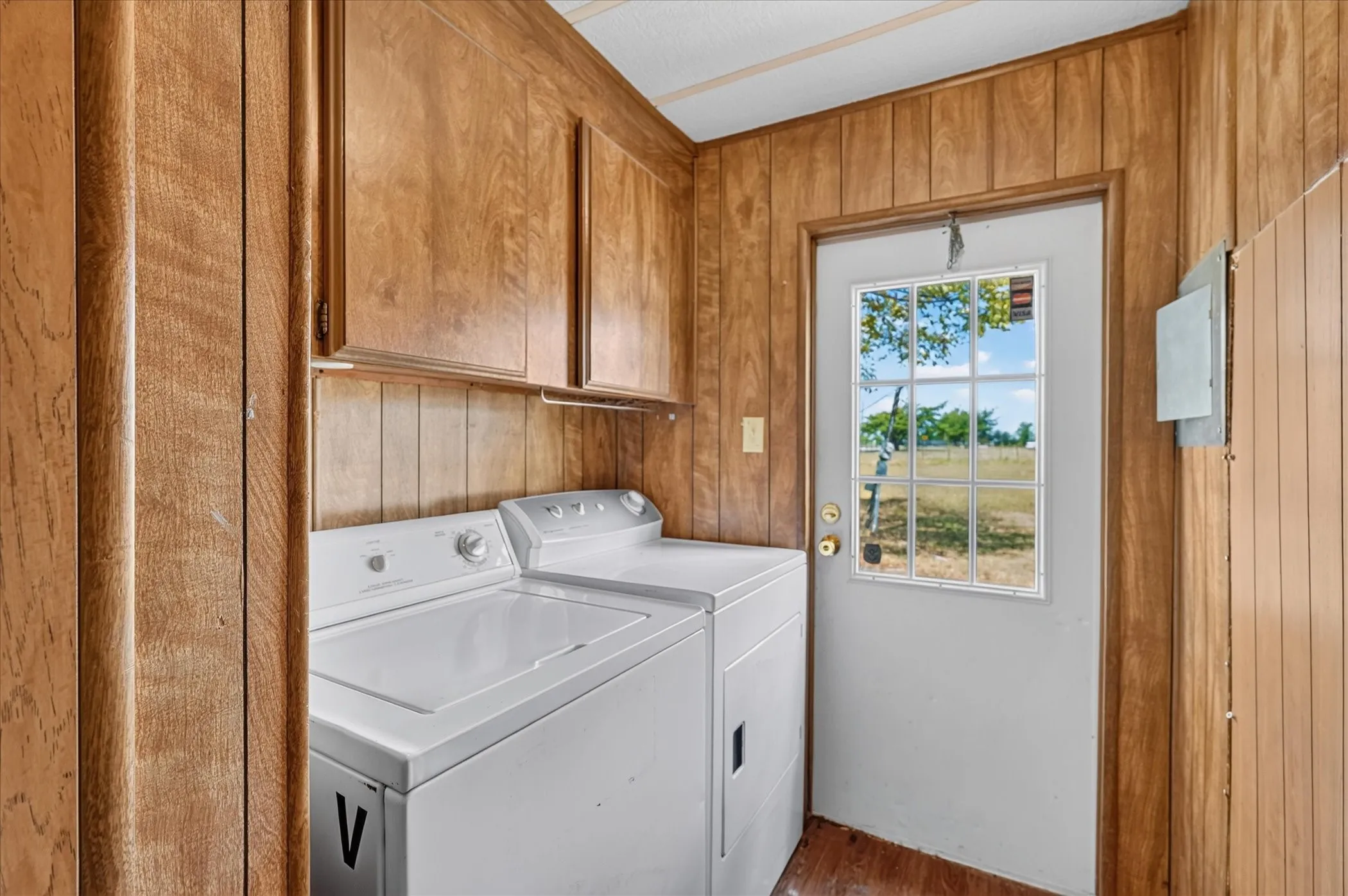 Dedicated laundry area with wood-finish paneling, overhead wood-finish cabinetry, and a white exterior door with a divided light window
