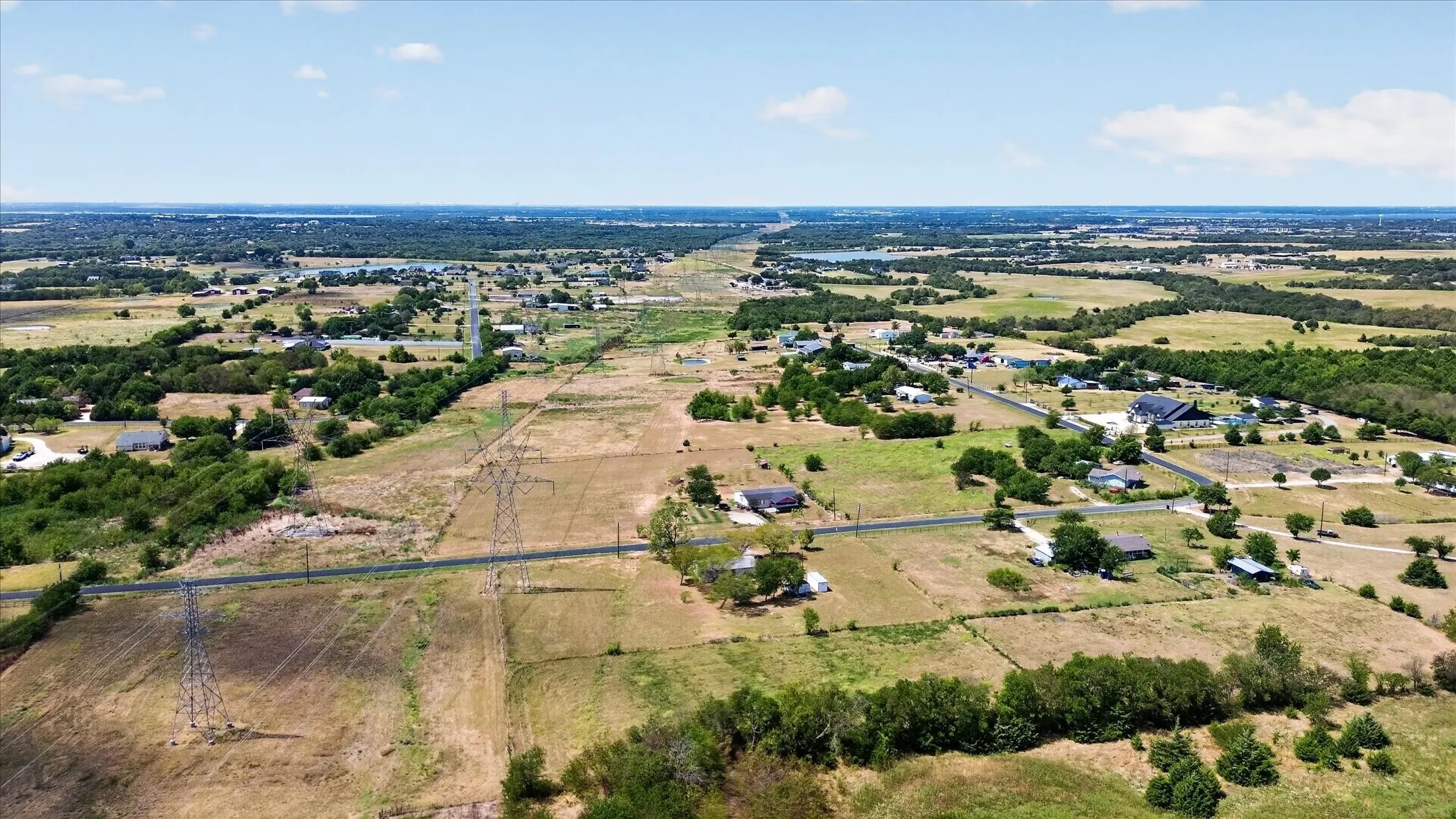 Expansive rural landscape featuring scattered residences, cultivated fields, and distant tree lines