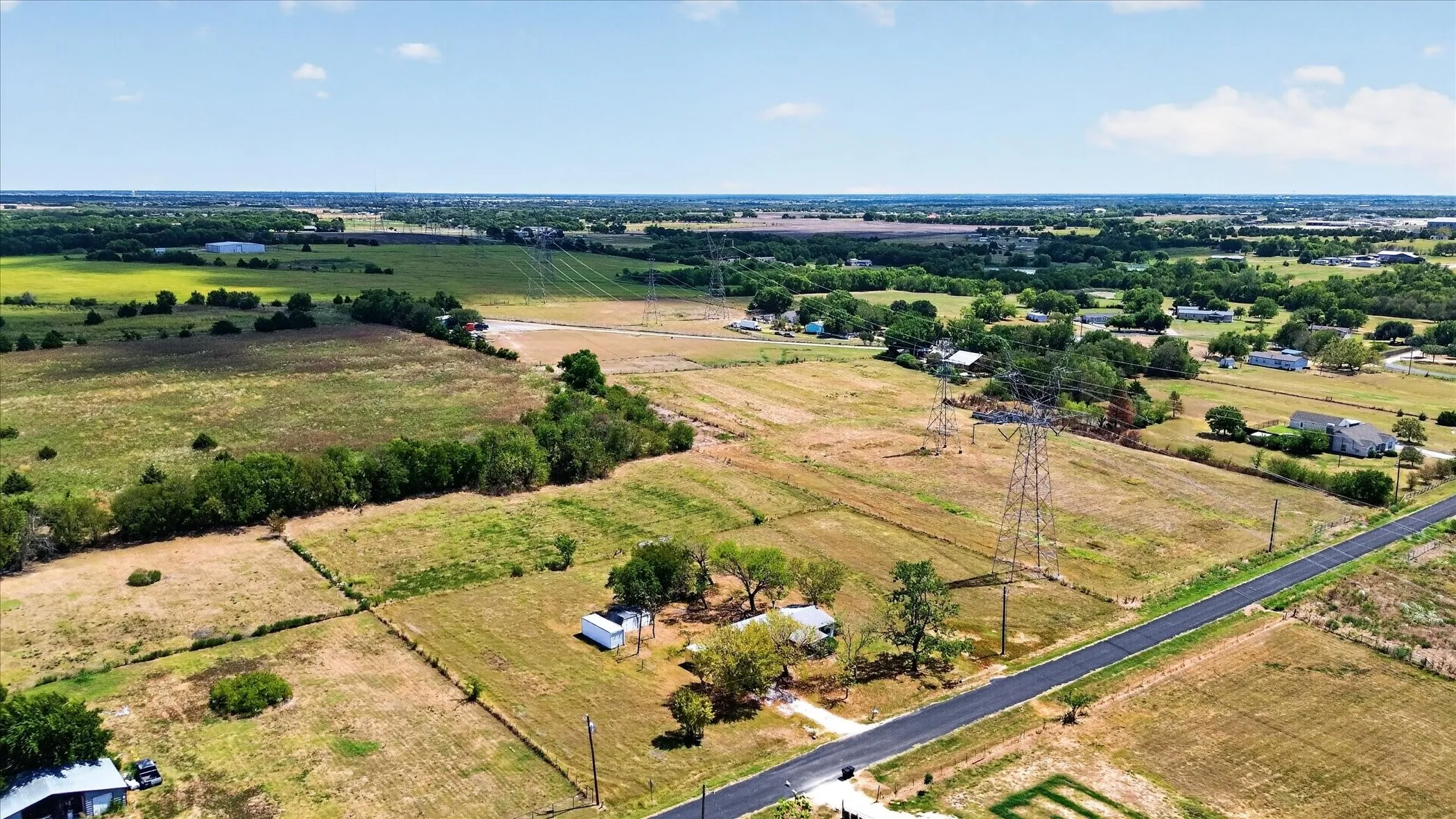 Expansive rural landscape featuring a paved road, scattered structures, and mature trees