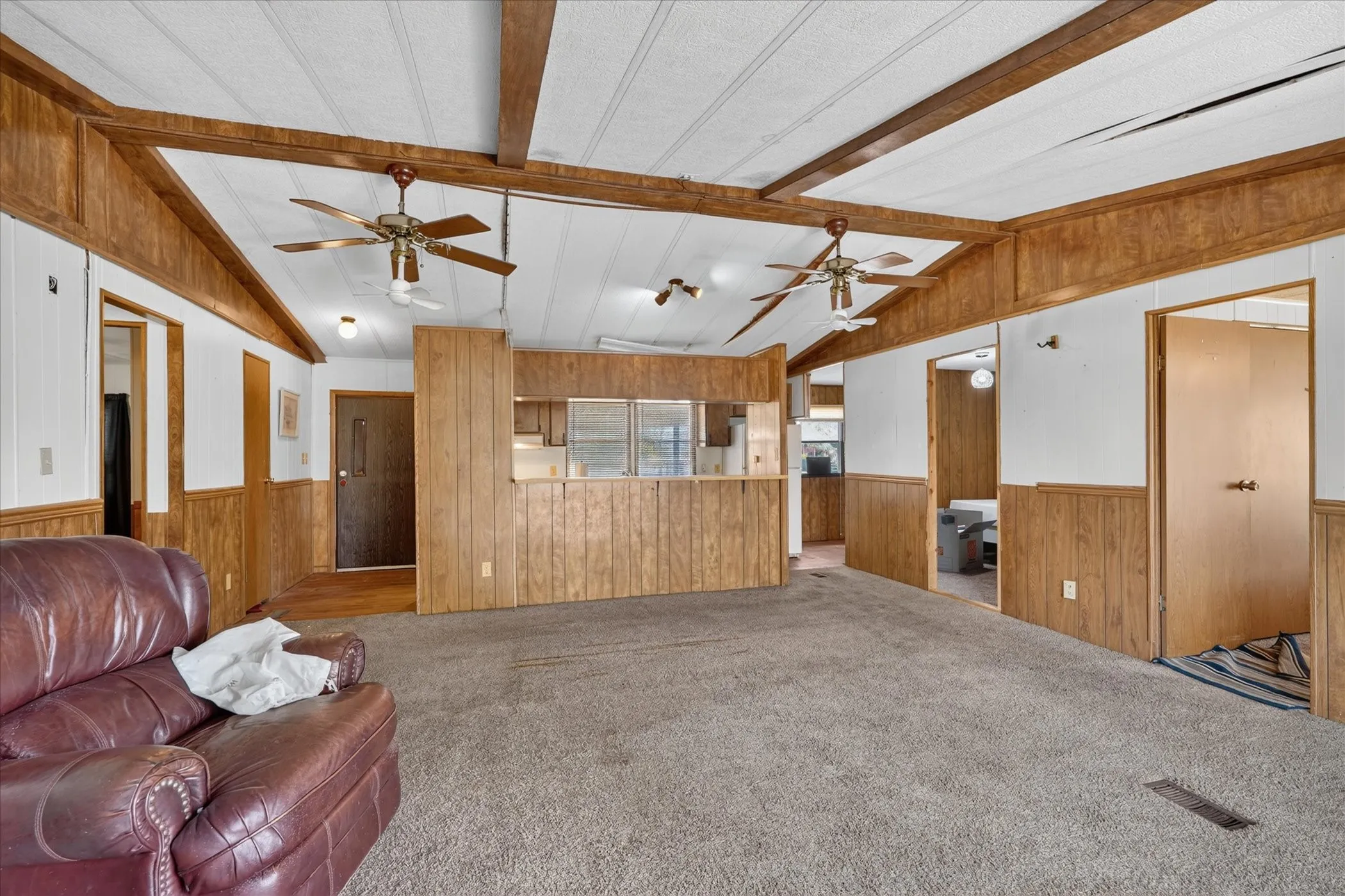 Vaulted ceiling with exposed wood beams, ceiling fans, wood-finish wall paneling, and wall-to-wall carpeting
