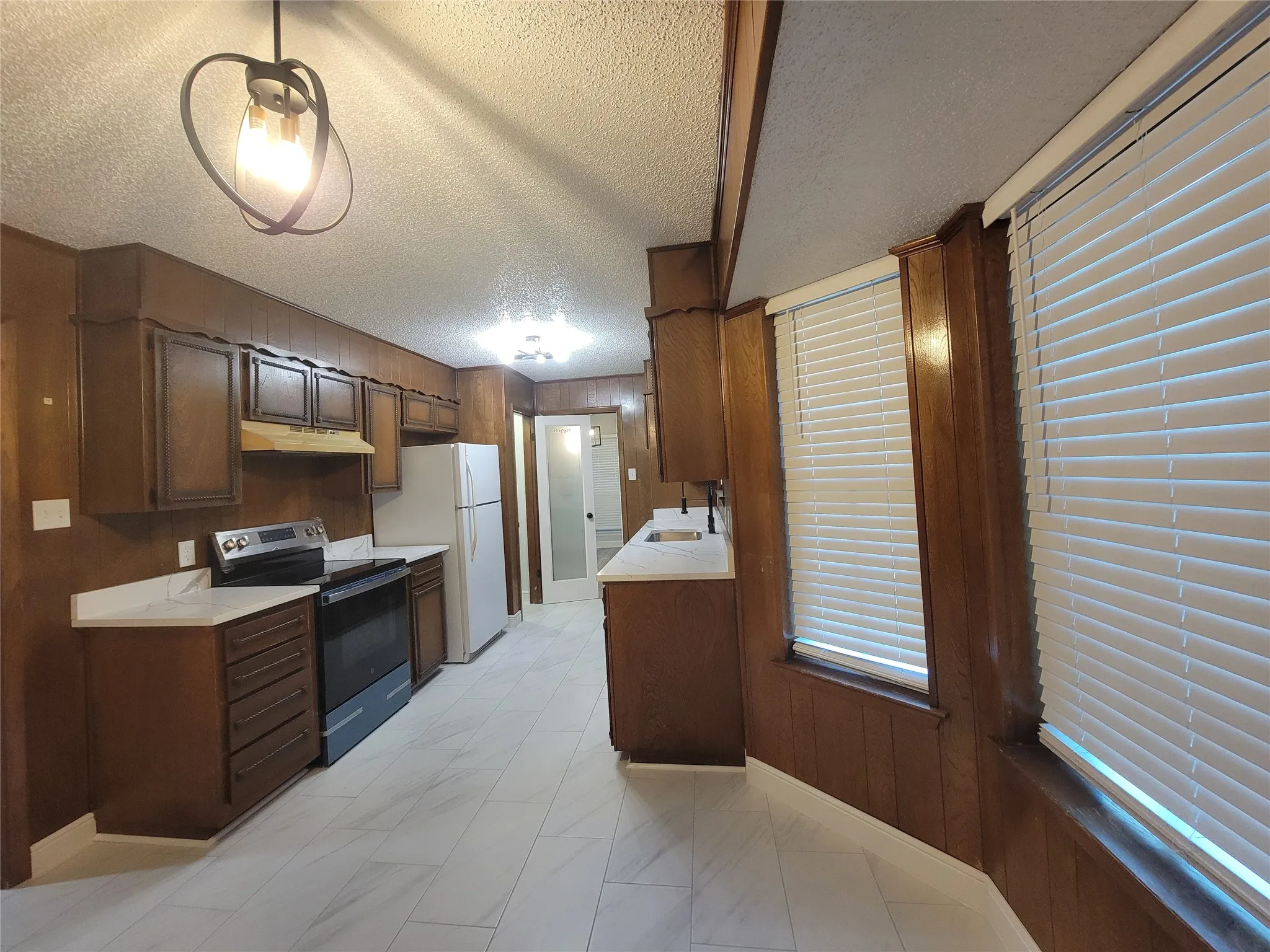 Wood paneling, bright white flooring, modern light fixture, white countertops, and white window blinds