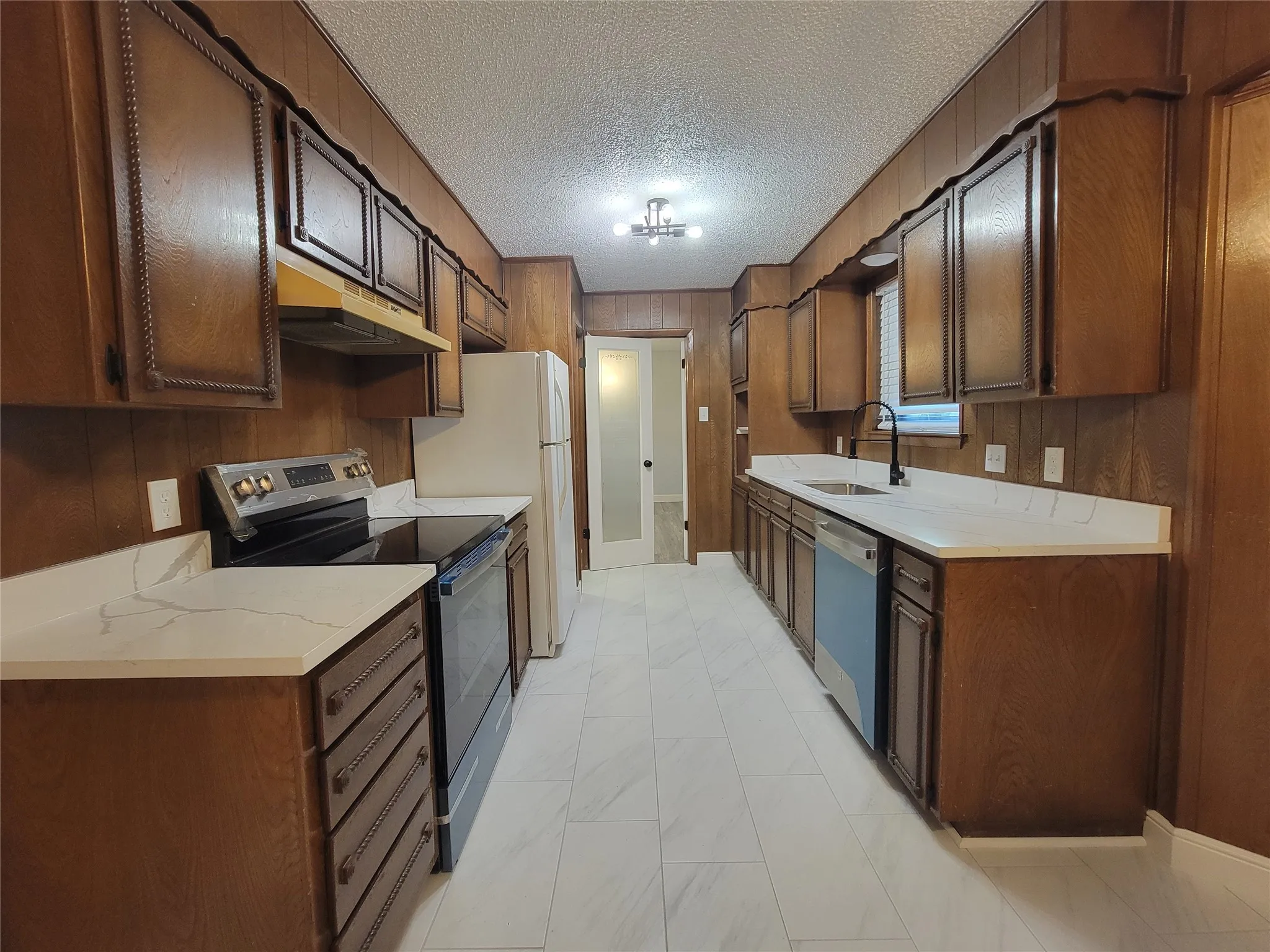 Kitchen with wood paneling, white countertops, built-in cabinetry, stainless steel appliances, and tile flooring