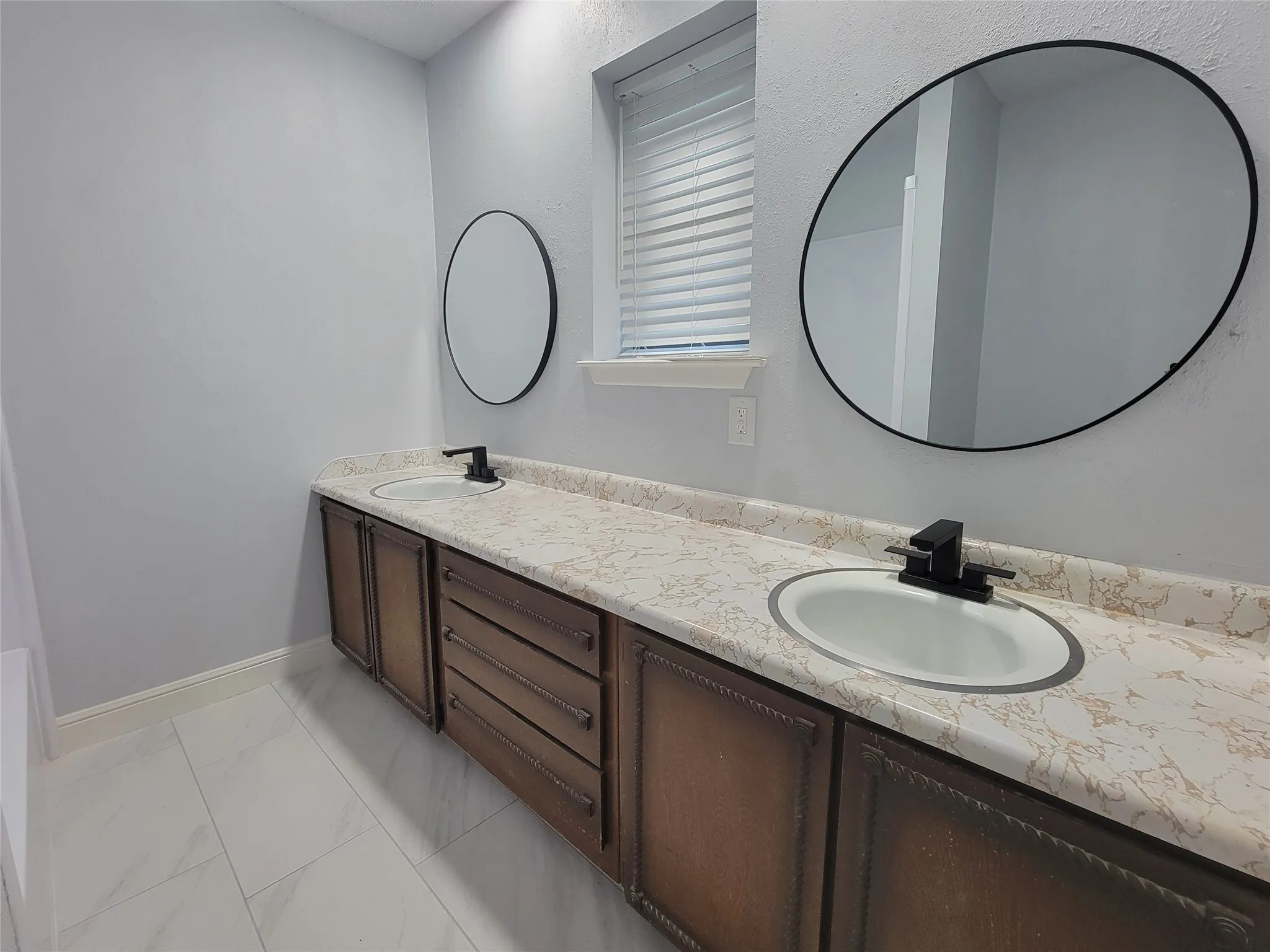Dual vanity with integrated sinks, patterned countertop, dark wood-finish cabinetry, and contemporary round mirrors