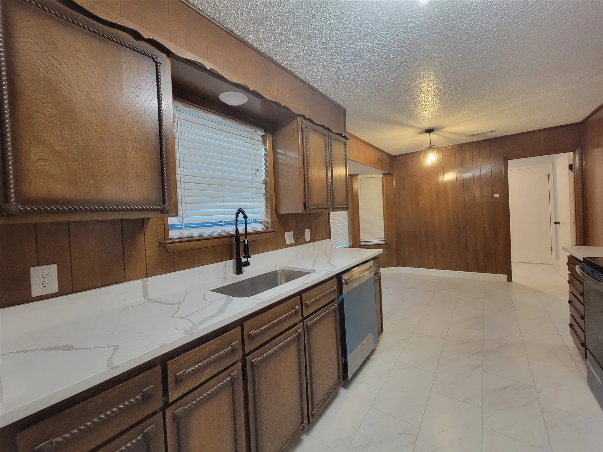 Kitchen featuring white stone-finish countertops, stainless steel undermount sink, matte black pull-down faucet, stainless steel dishwasher, and white tile flooring