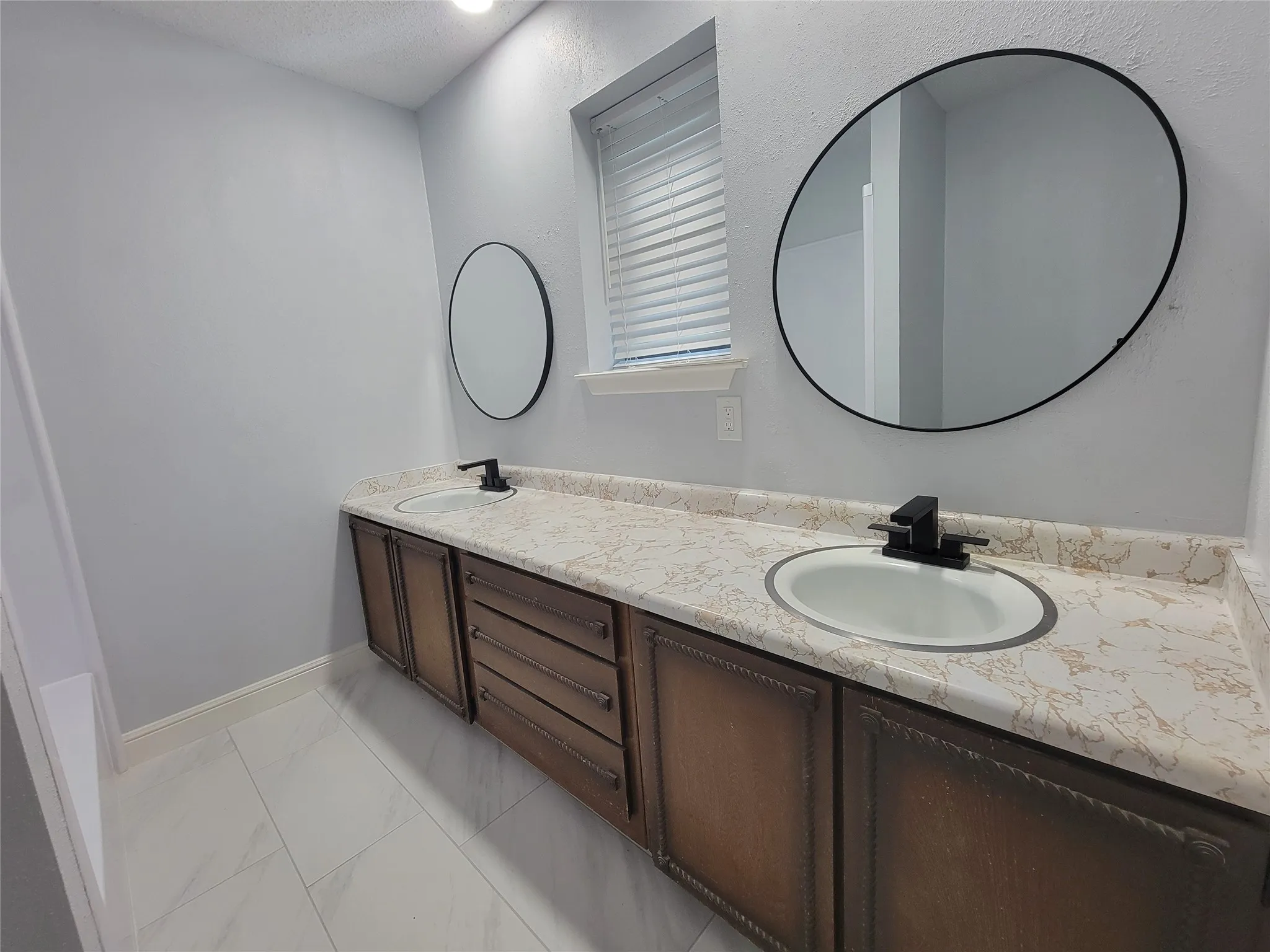 Dual vanities with matte black fixtures, round mirrors, and a light-colored countertop