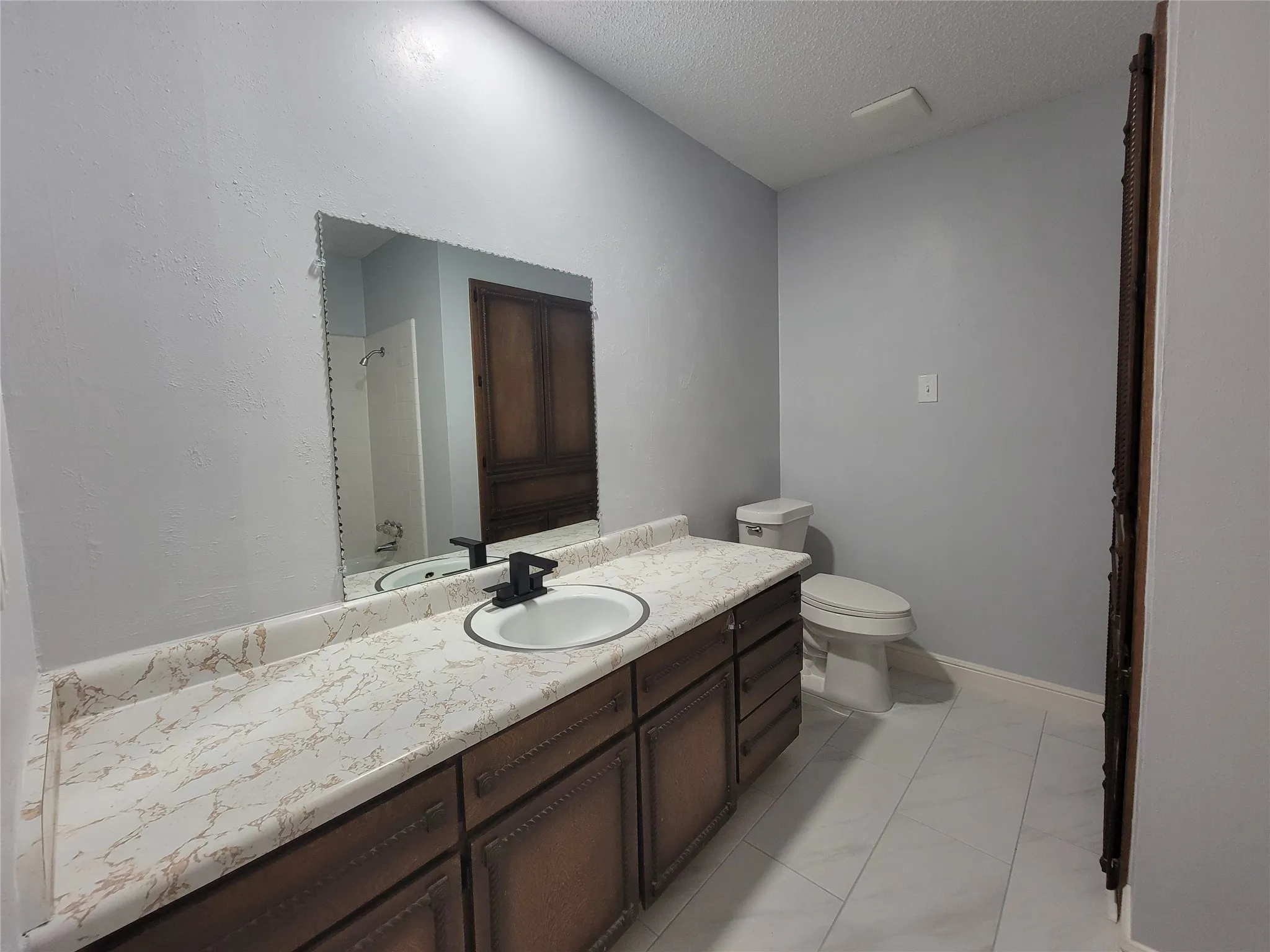 Vanity with a single basin, dark wood-finish cabinetry, and a light-toned countertop