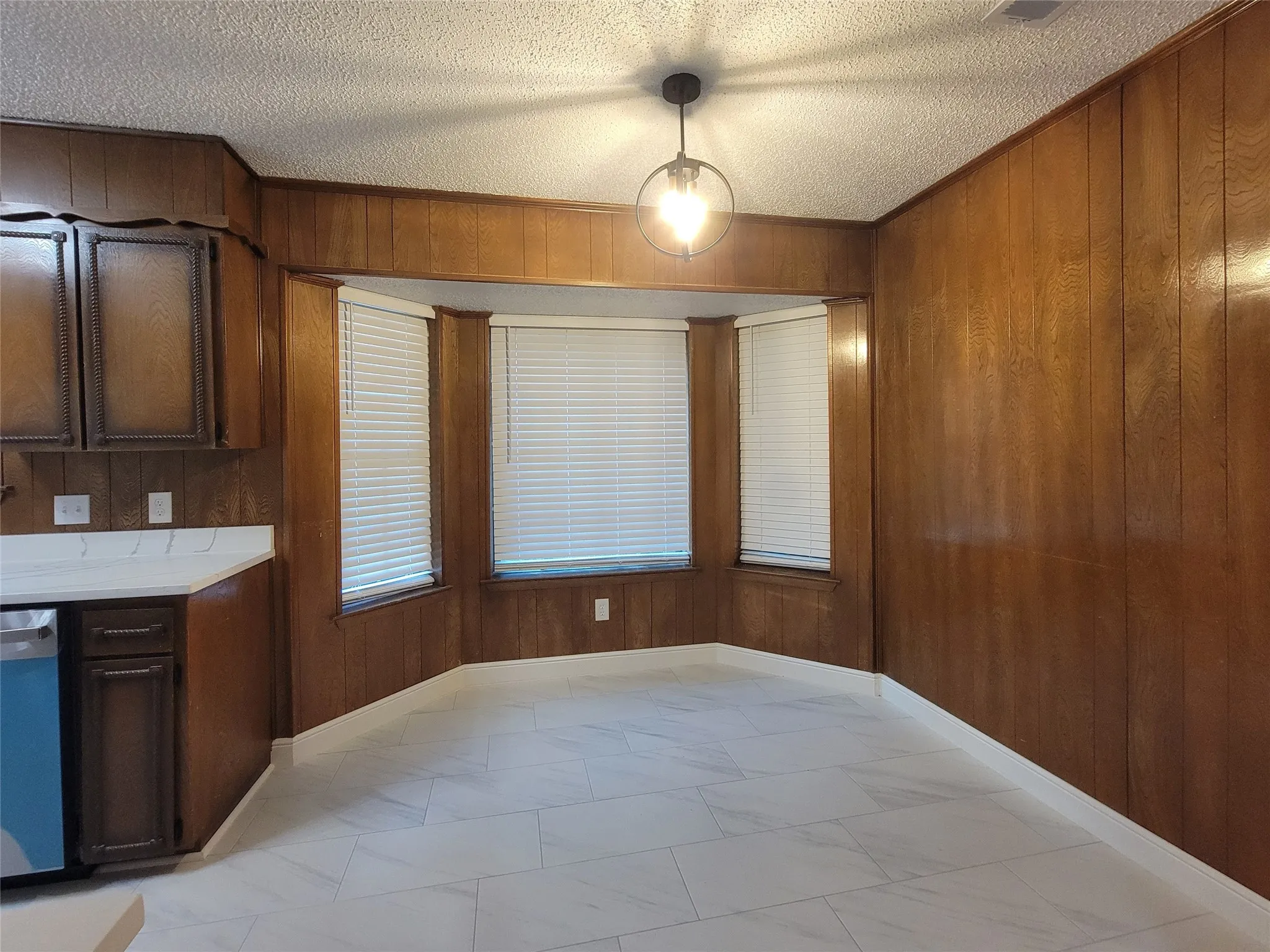 Bay window with blinds, wood paneling, white countertop, and white tile flooring
