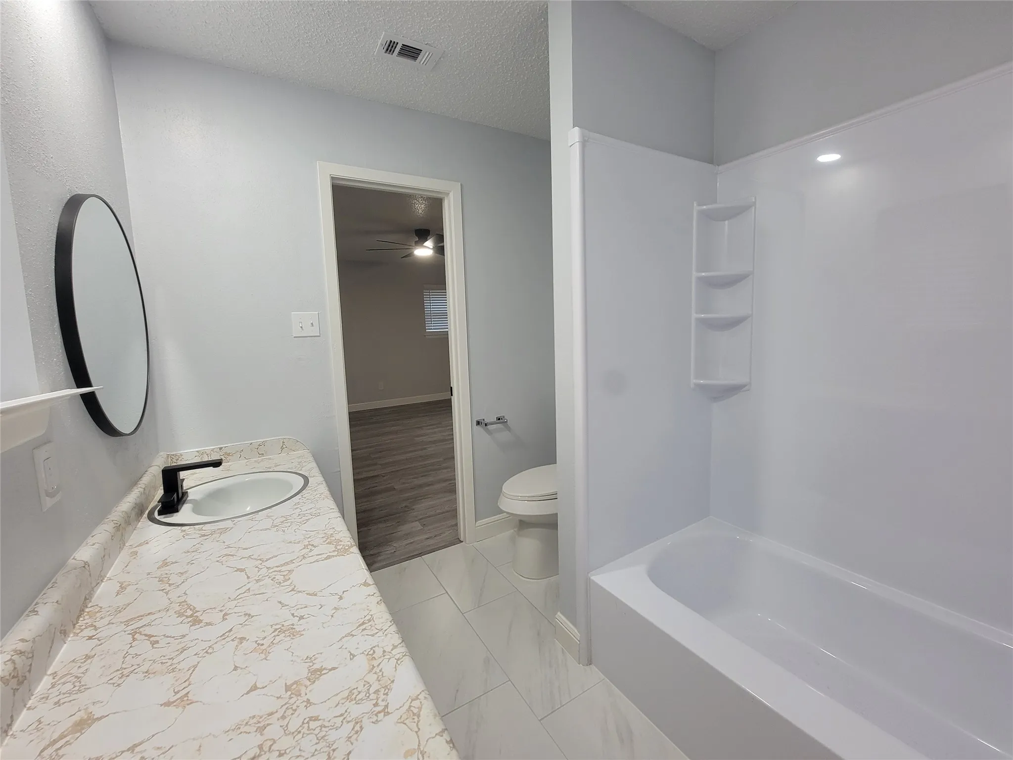 Bathroom featuring a white bathtub, integrated shelving, vanity with a white oval sink, and a black-framed circular mirror