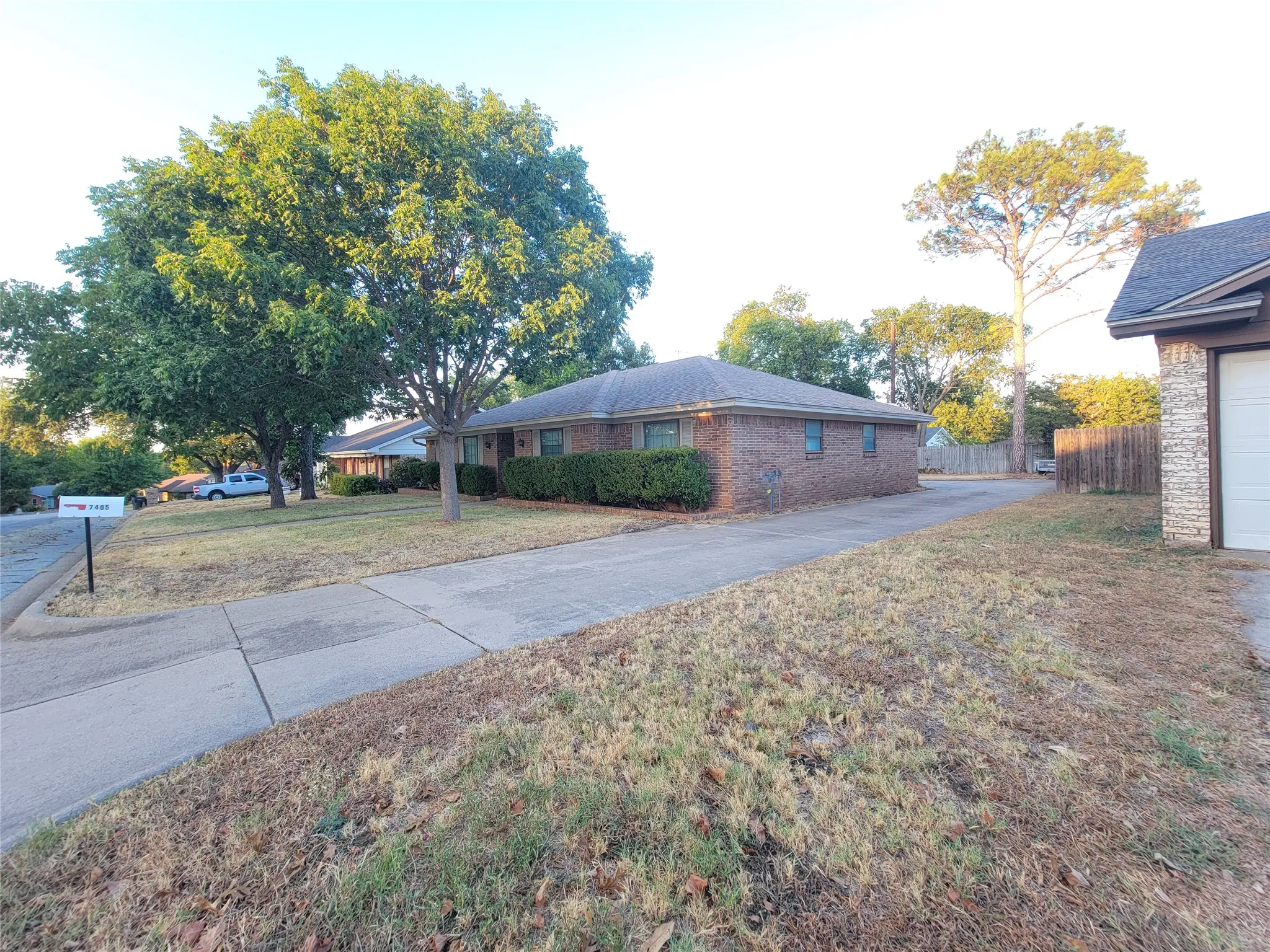 Brick exterior, mature trees, concrete driveway, wood privacy fence, attached garage