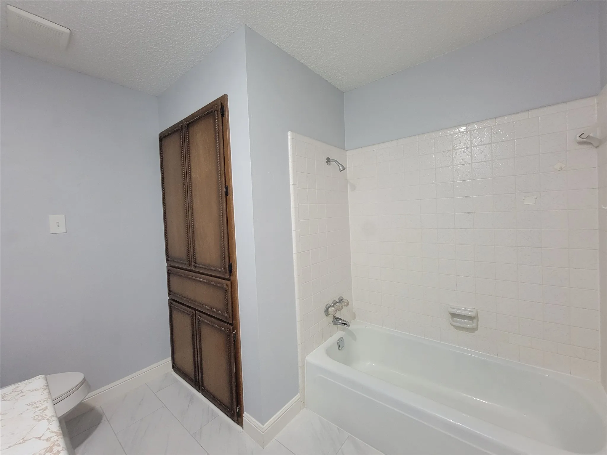 Built-in wood-finish cabinetry, white tiled tub surround, white bathtub, and wood-finish flooring