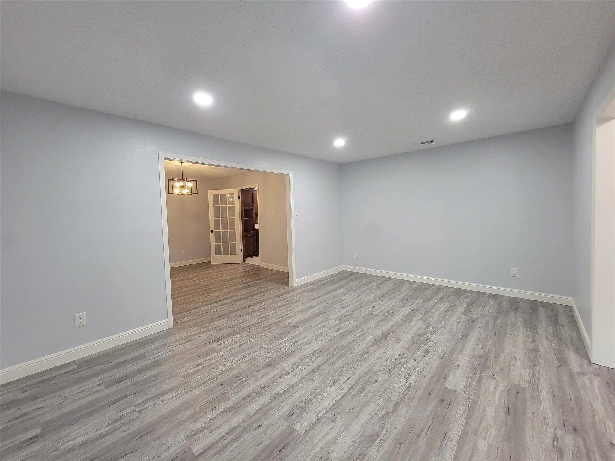 Recessed ceiling lighting, wood-finish flooring, light gray wall finishes, white trim, and a French door entry