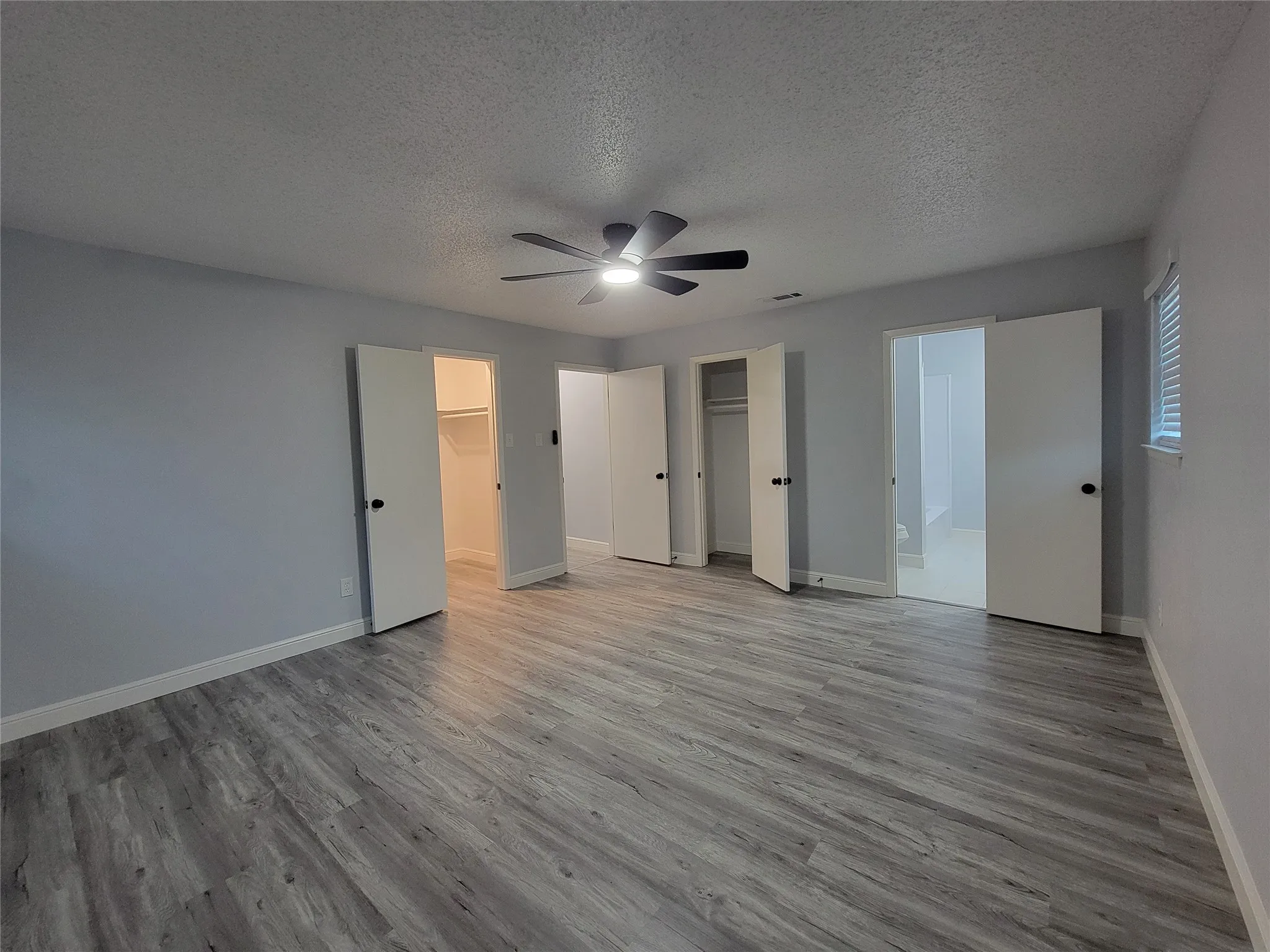 Spacious room with wood-finish flooring, light gray walls, and a ceiling fan